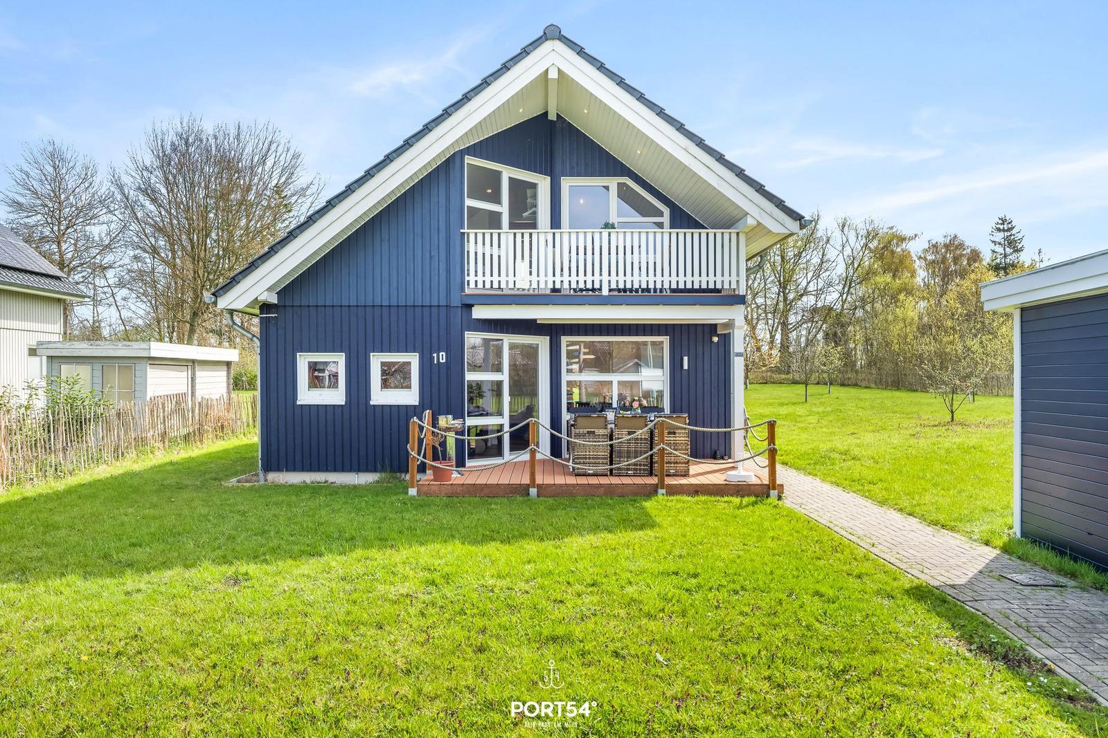 Blau gestrichenes Haus mit Balkon und Terrasse auf grünem Grundstück.