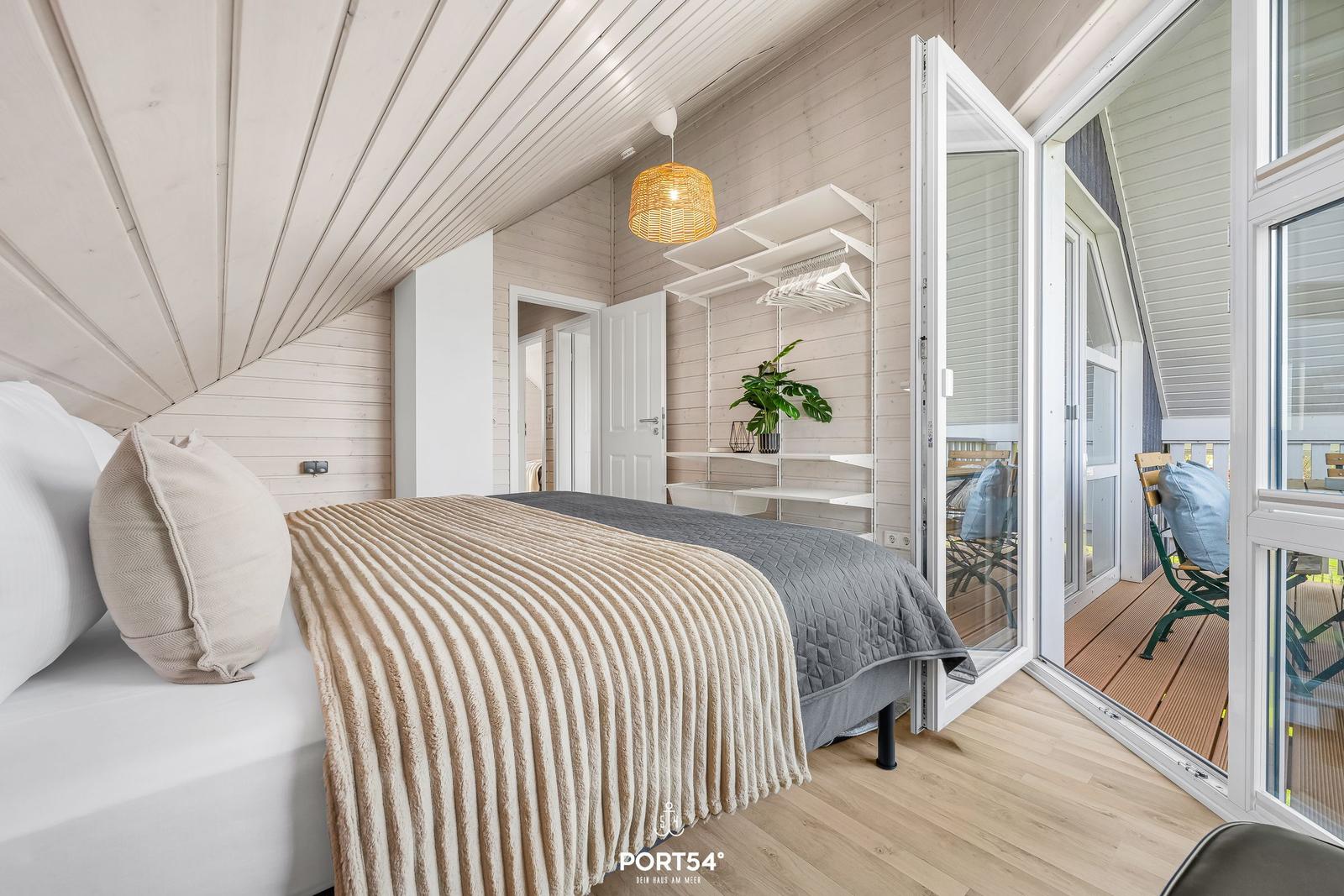 Schlafzimmer mit Bett, Schrank und Balkonanschluss. Holzwände und Dachschrägen.