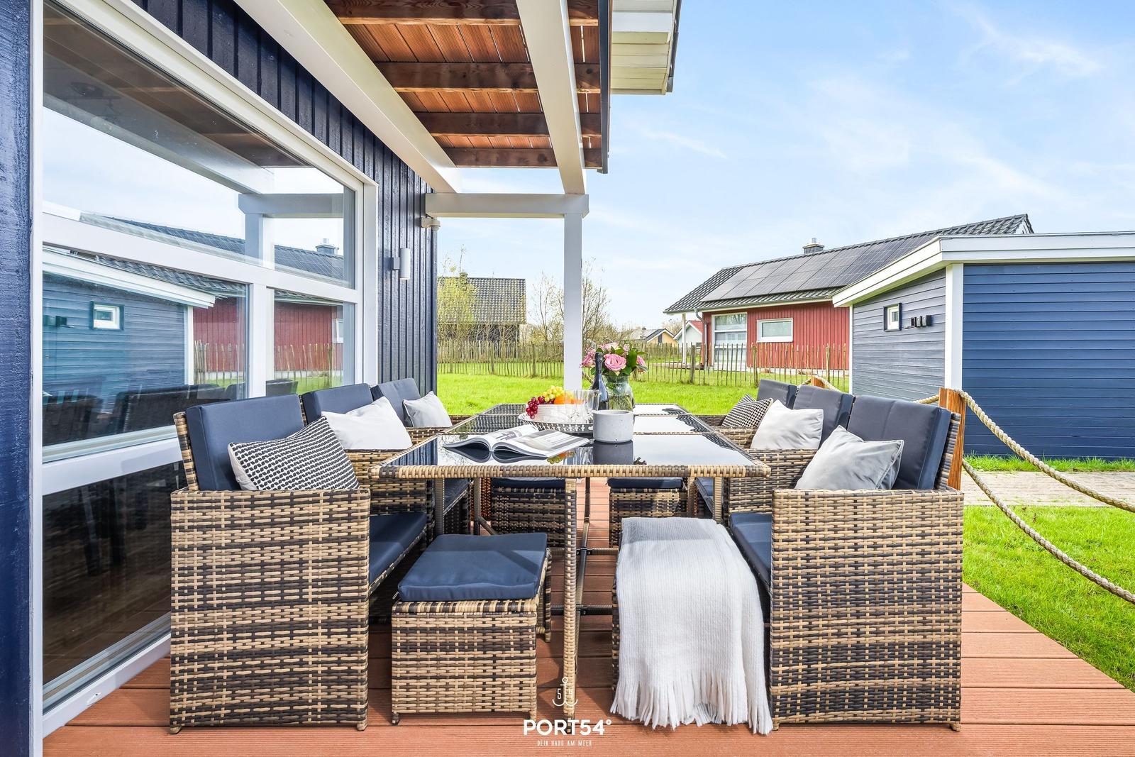 Terrasse mit Sitzgruppe, Tisch und Blumen. Holzdecke und Gartenblick.