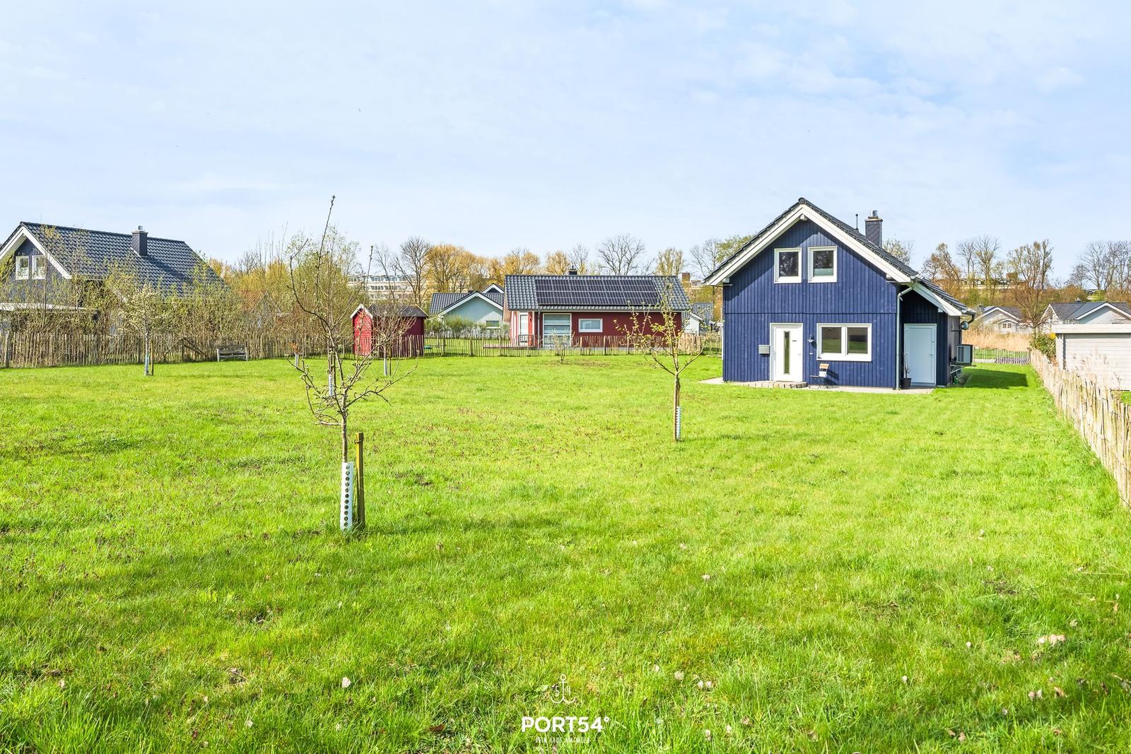 Ein blaues Haus mit weißem Fensterrahmen steht auf einer grünen Wiese.