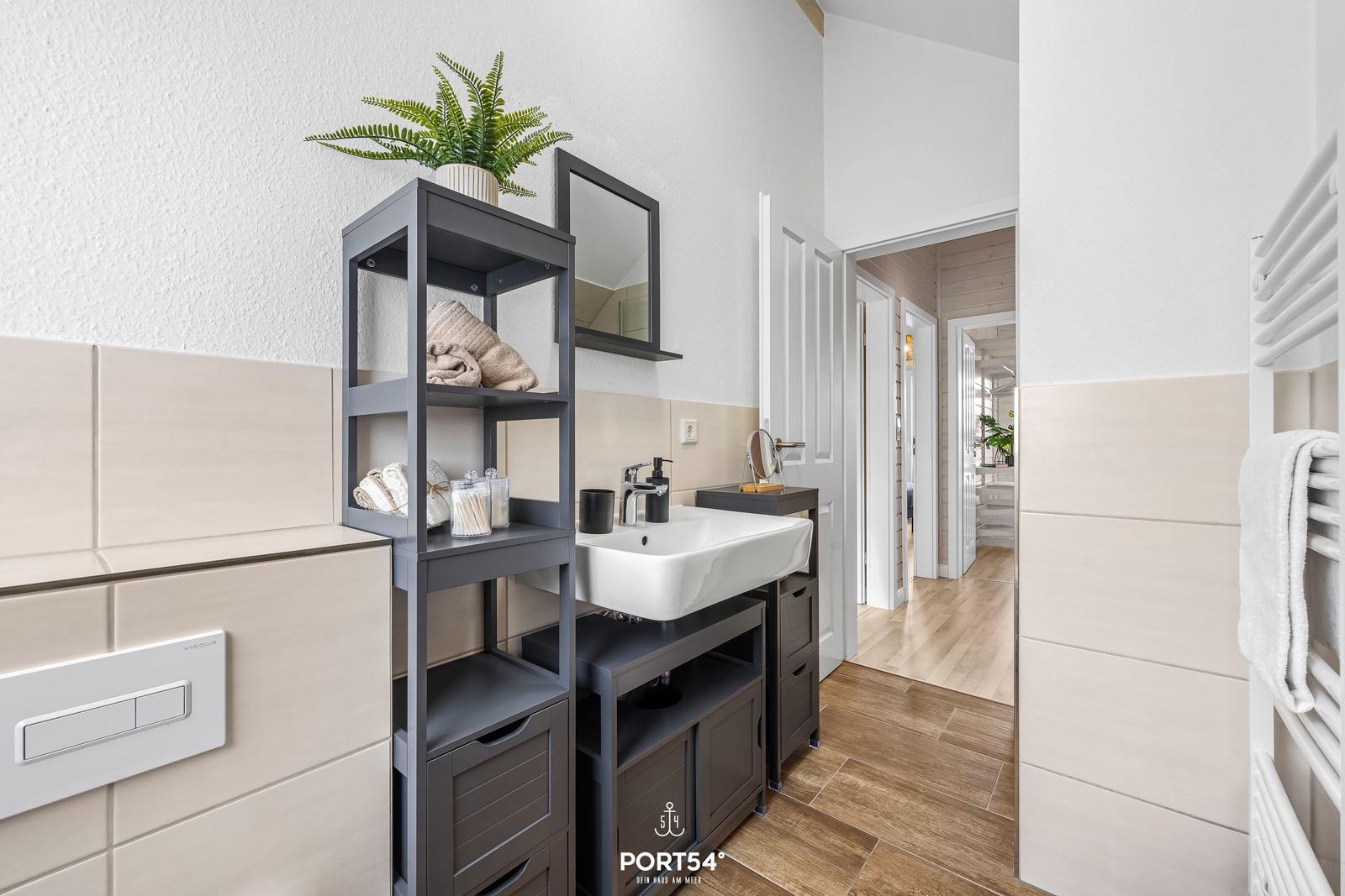 Badezimmer mit Waschbecken, Regal und Heizung. Holzboden und hellbeige Fliesen.
