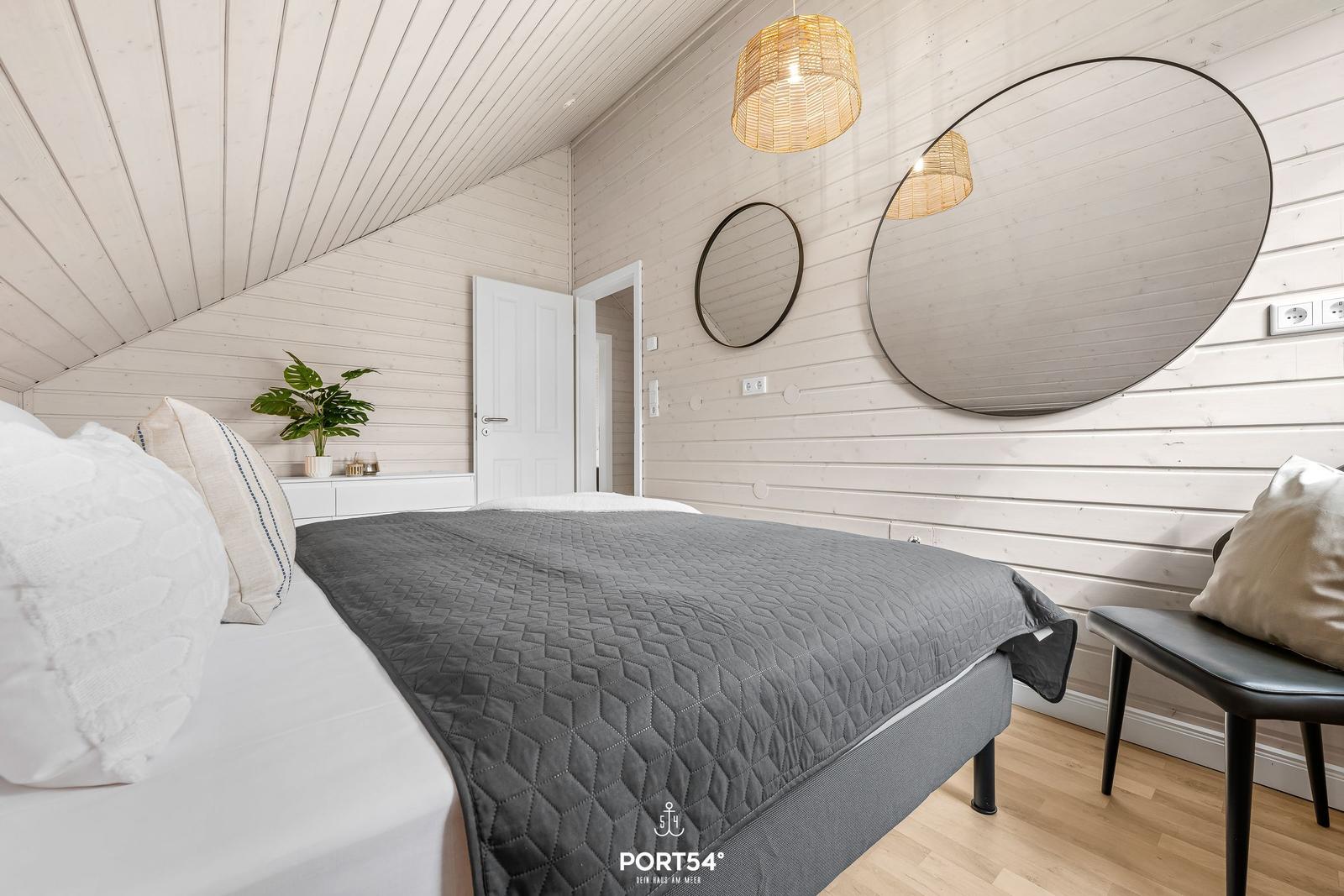 Schlafzimmer mit Bett, Wandspiegel und Deckenleuchte.
