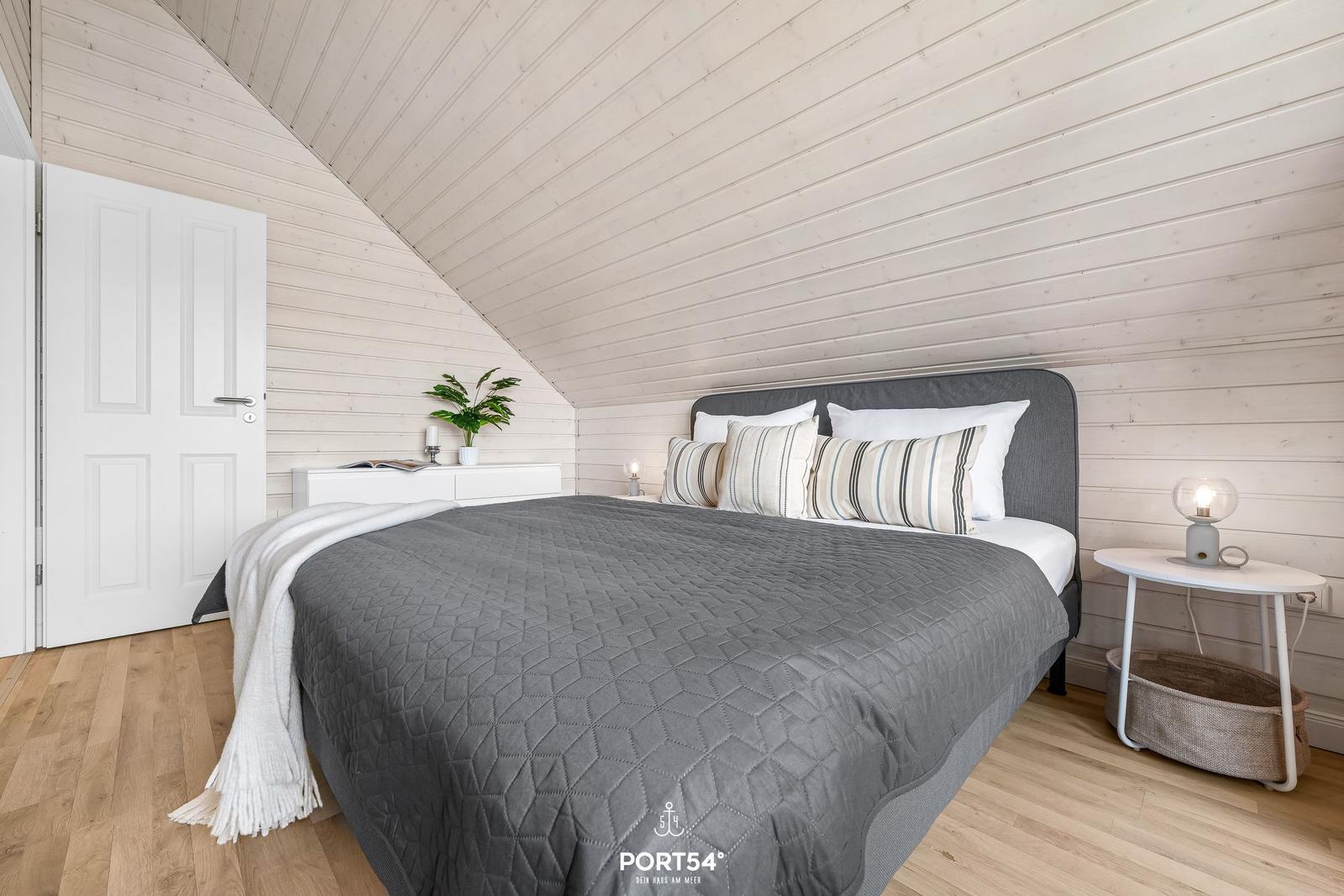 Schlafzimmer mit Dachschrägen, Bett, Nachttisch und Pflanze.