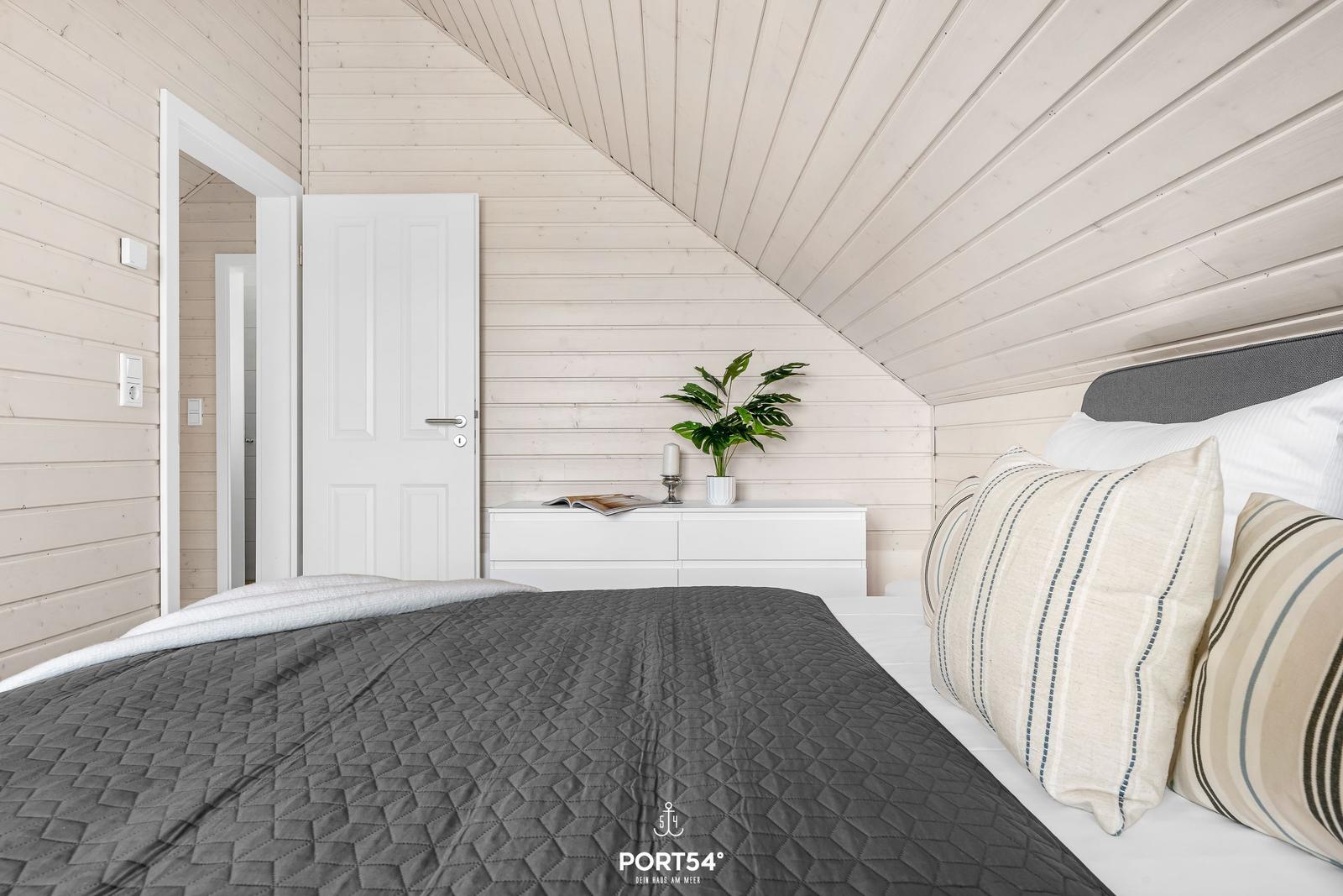 Schlafzimmer mit Bett, Schrank und Pflanze an der Wand.