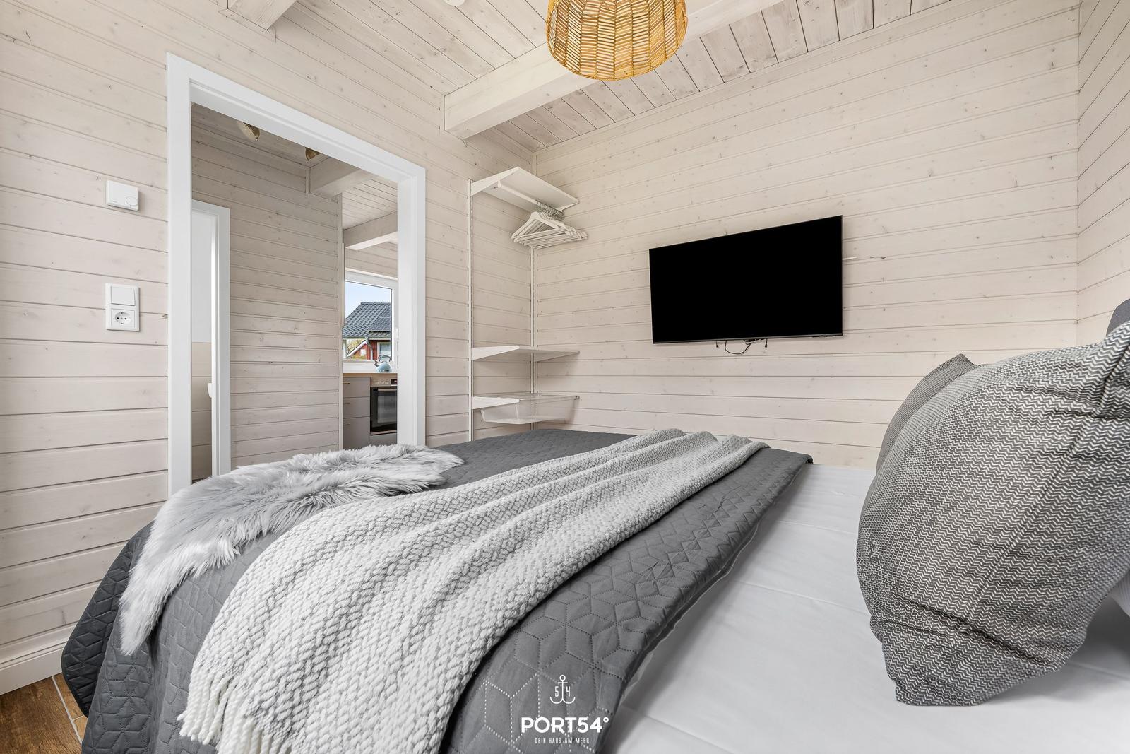 Schlafzimmer mit Bett, Wandfernseher und Holzwandverkleidung.