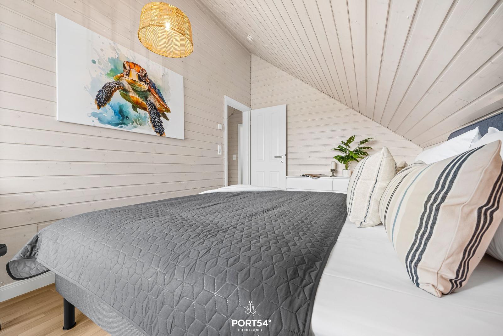 Schlafzimmer mit Bett, Wandbild und Deckenleuchte. Holzwände und schräge Decke.