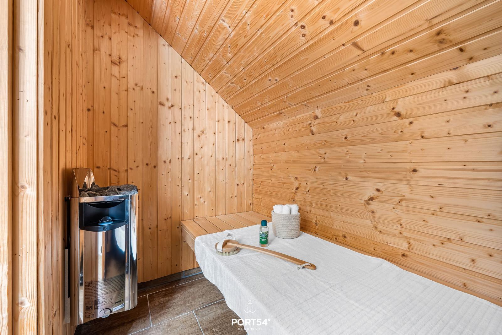 Sauna mit Holzwand, Liege, Dampferzeuger und Badematten.