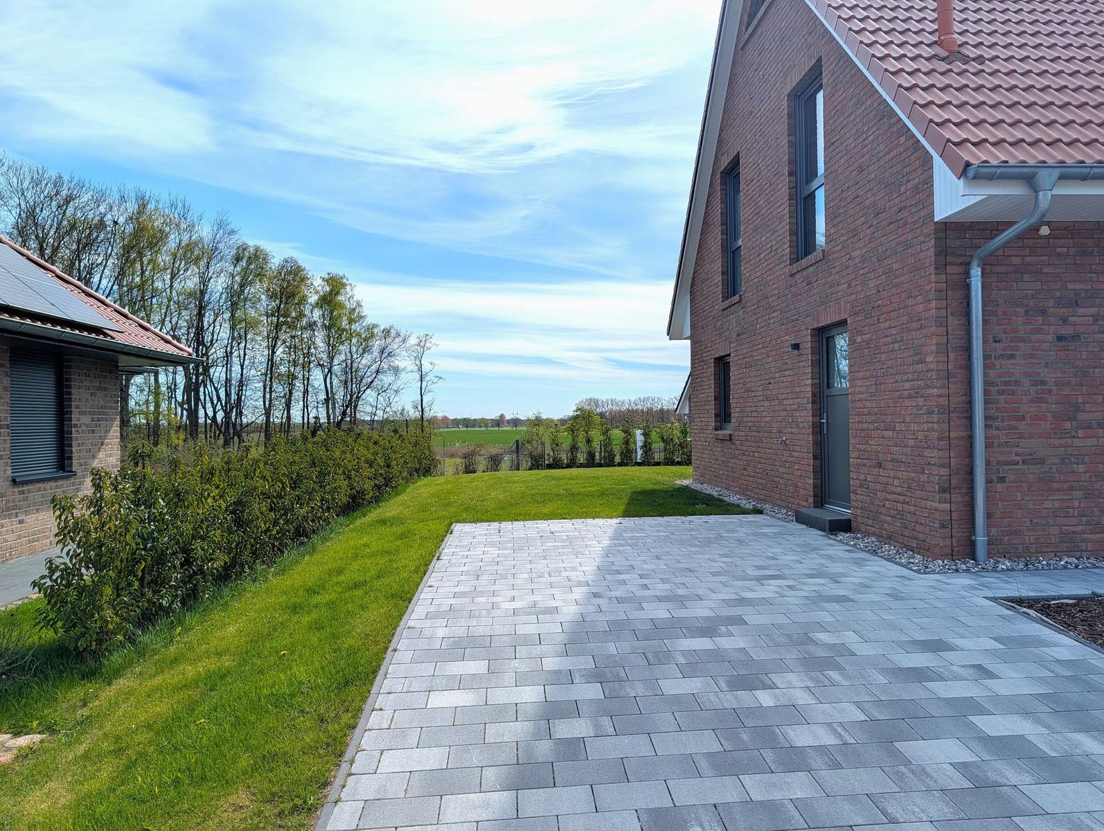 Haus mit gepflastertem Hof, Rasenfläche und Blick auf Felder.
