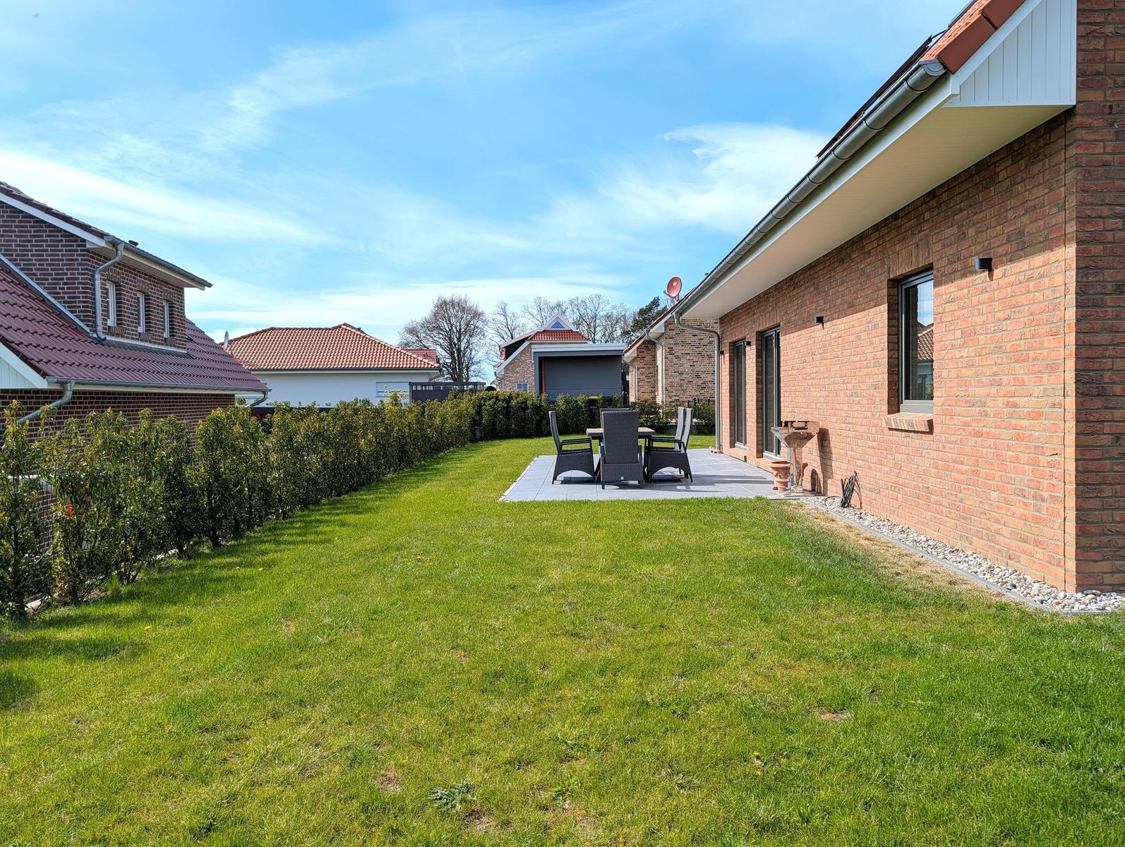 Hinterhof mit Rasenfläche, Terrasse und Gartenmöbeln an einer Backsteinmauer.