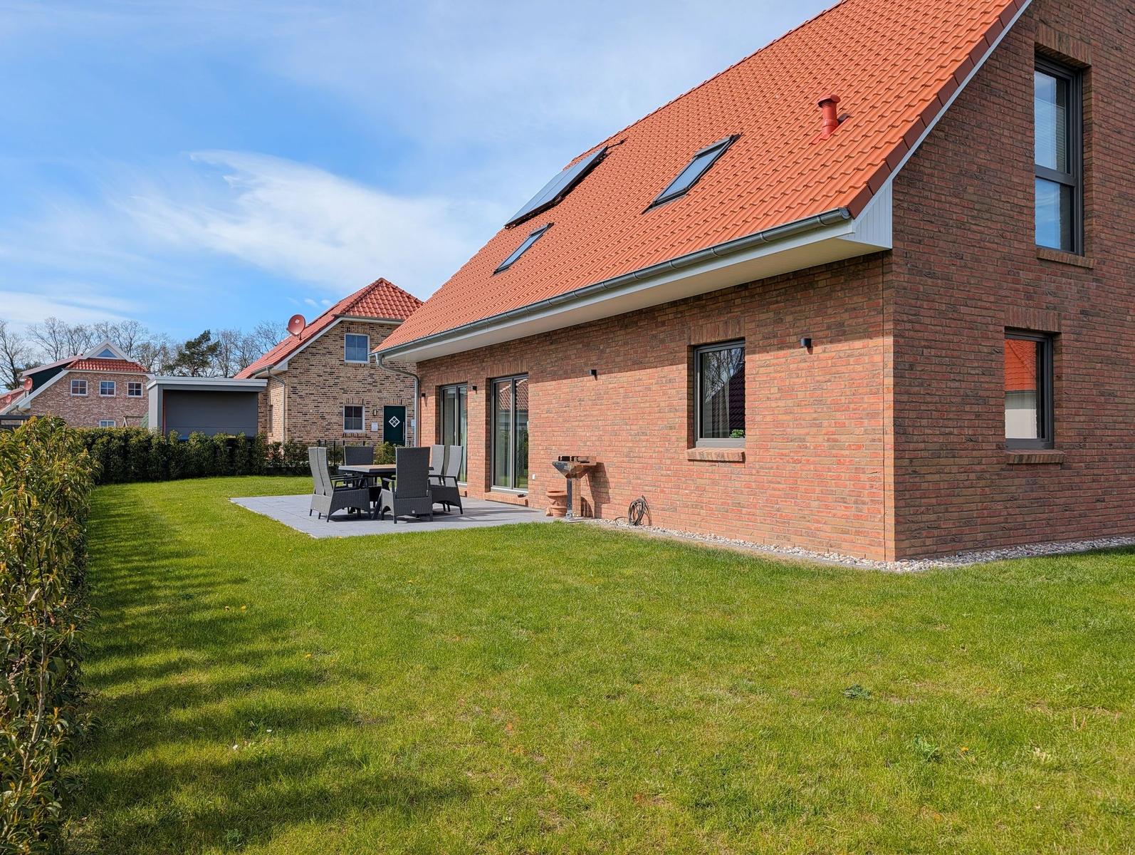 Rotes Ziegeldach, Garten mit Tisch und Stühlen, moderne Fenster, Grillplatz.