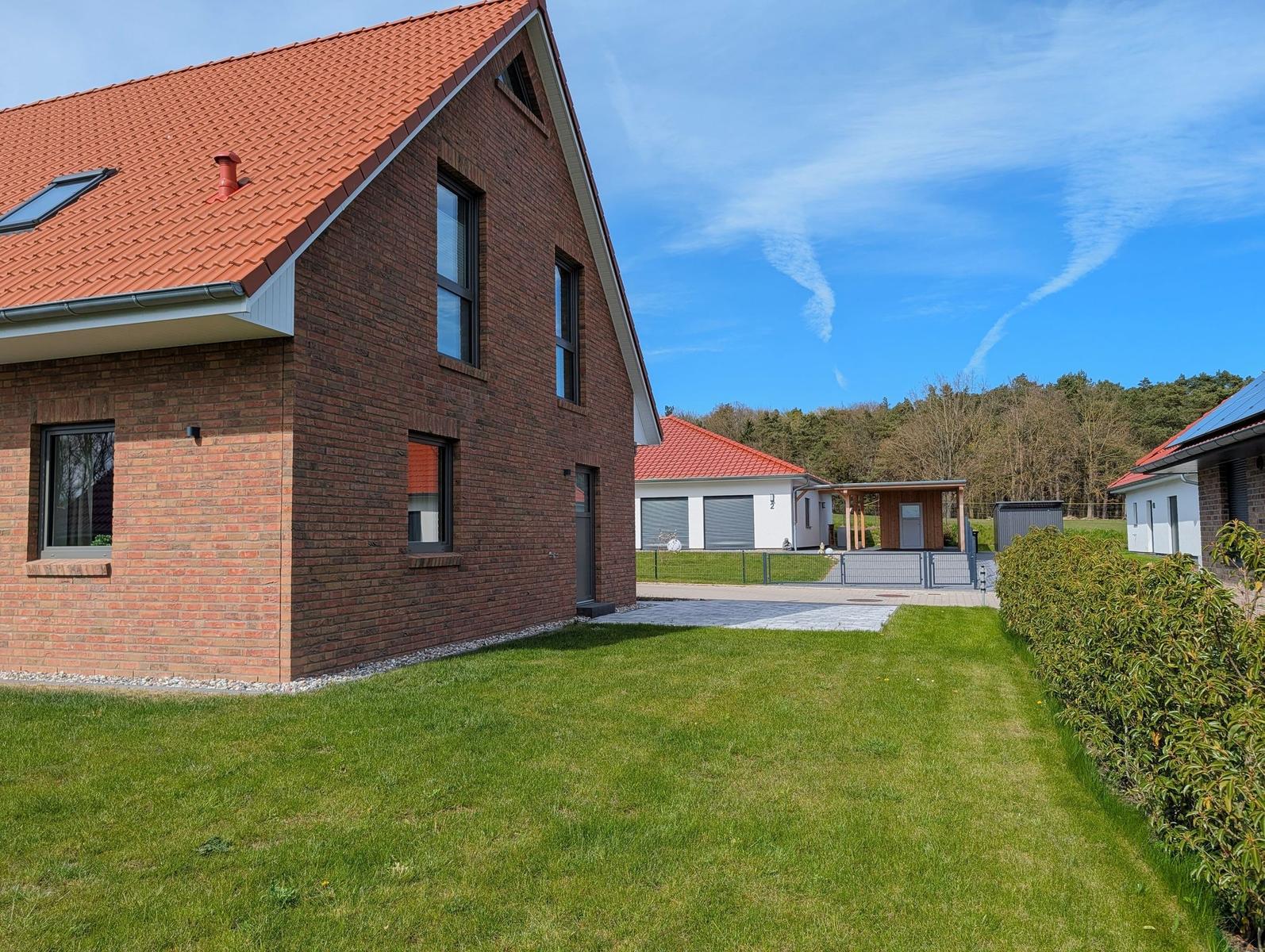 Rotes Dach, Backsteinhaus mit grünem Rasen und Wald im Hintergrund.