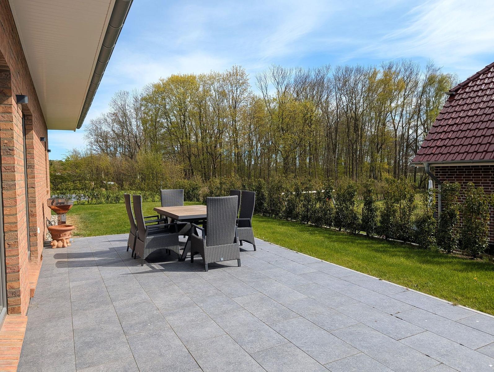 Terrasse mit Tisch und Stühlen, umgeben von Grün und Bäumen.