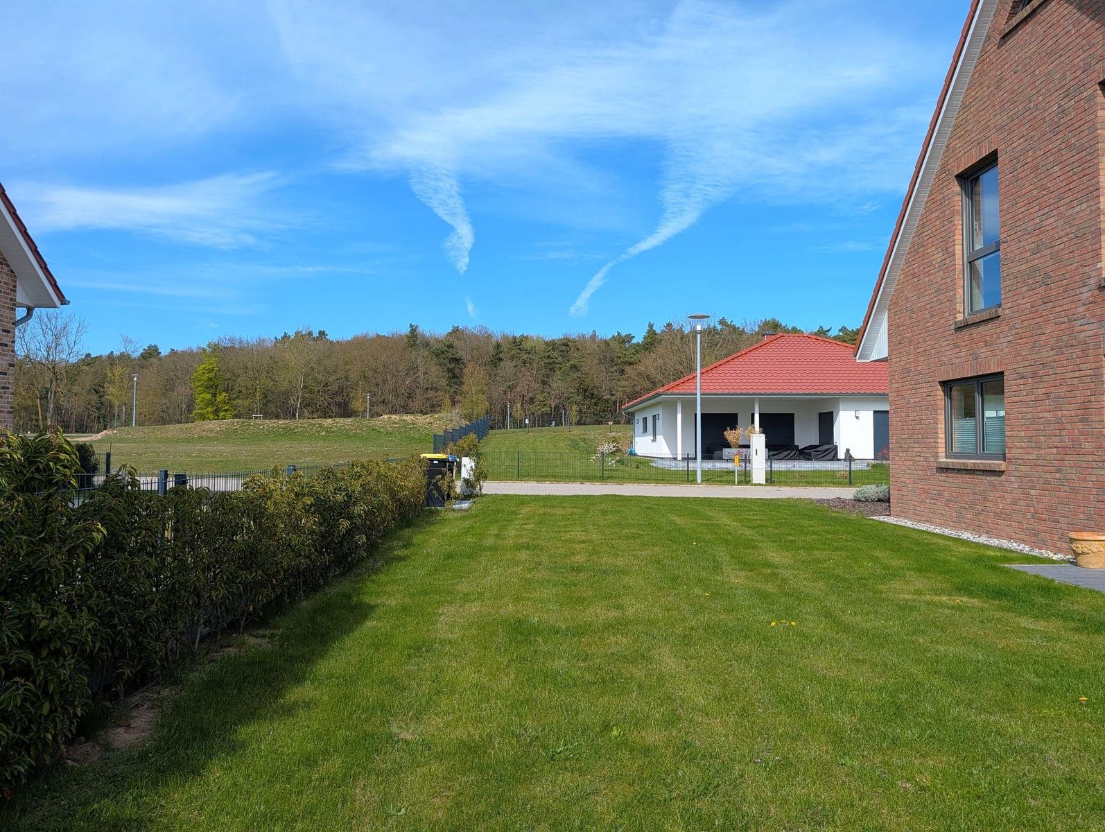 Grüner Rasenbereich mit Blick auf eine weiße Villa mit rotem Dach und Wald im Hintergrund.
