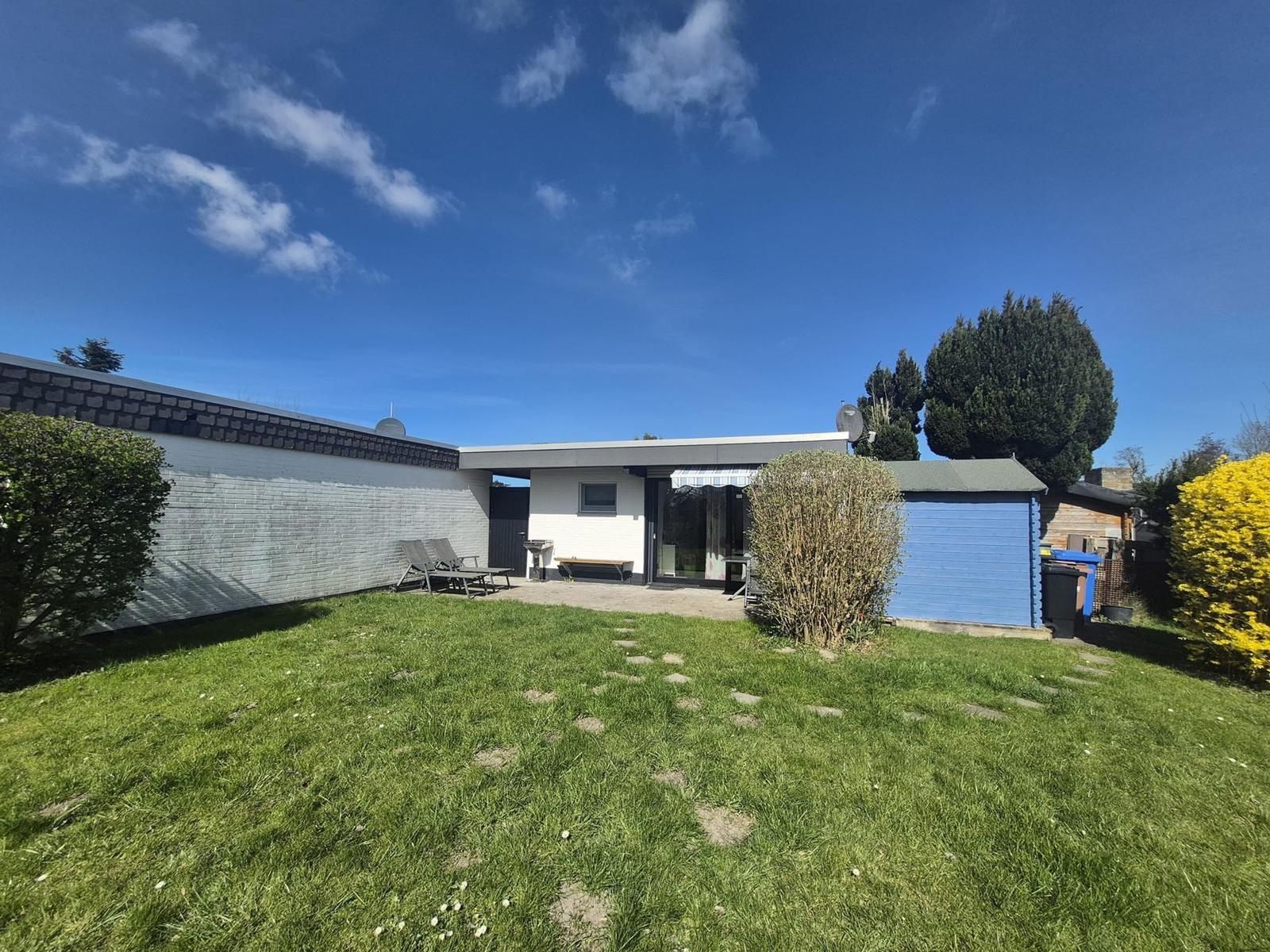 House with garden, sun loungers, and blue shed under blue sky.