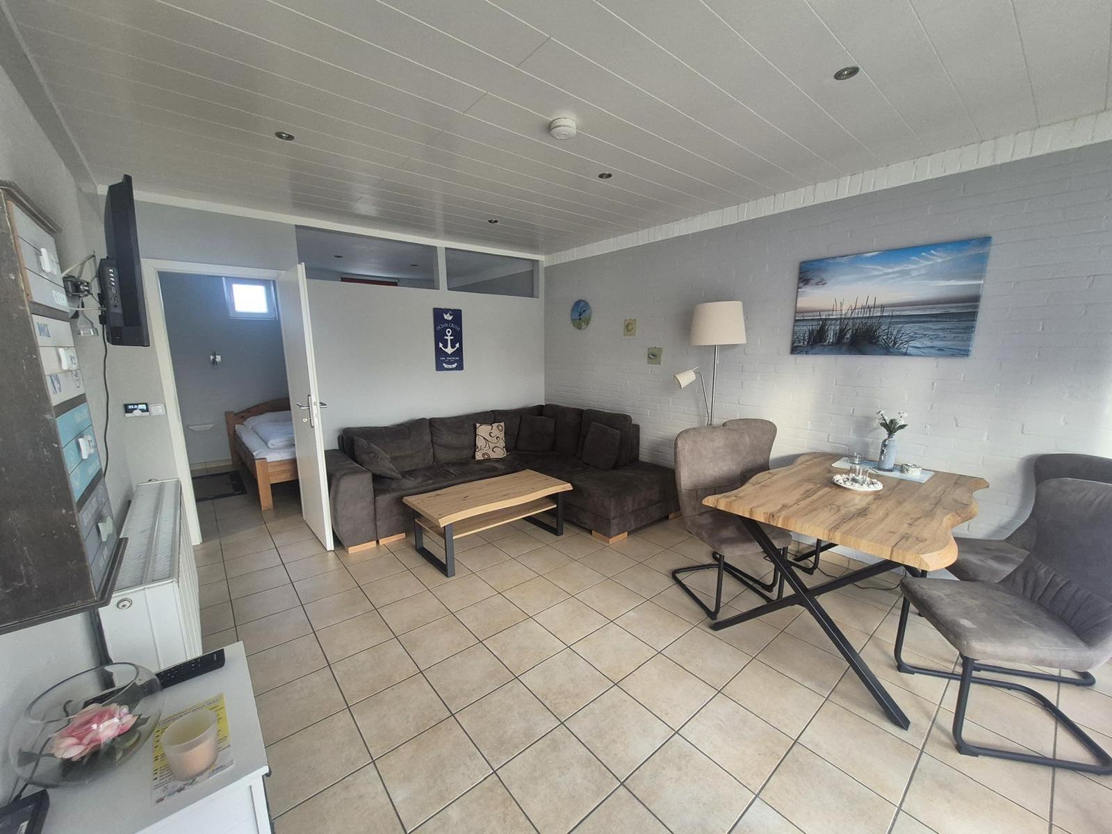 Living and dining area with sofa, table, and chairs. A bedroom is visible in the background.