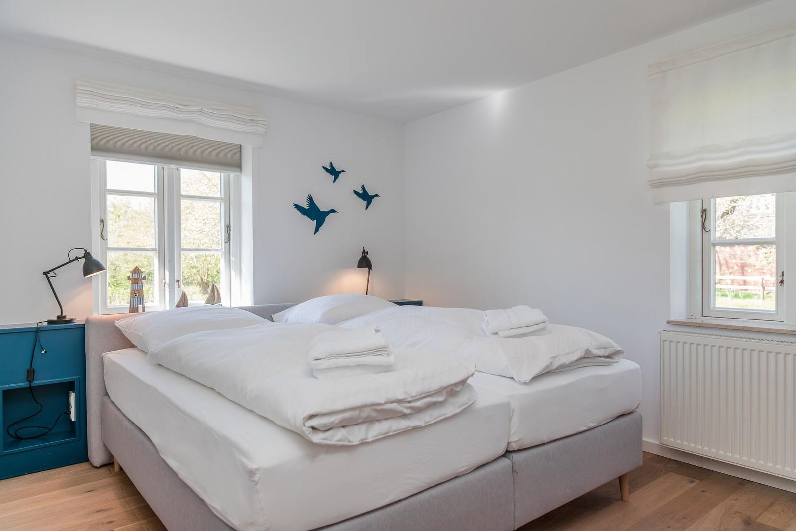 Schlafzimmer mit Doppelbett, zwei Fenstern und Wanddekoration