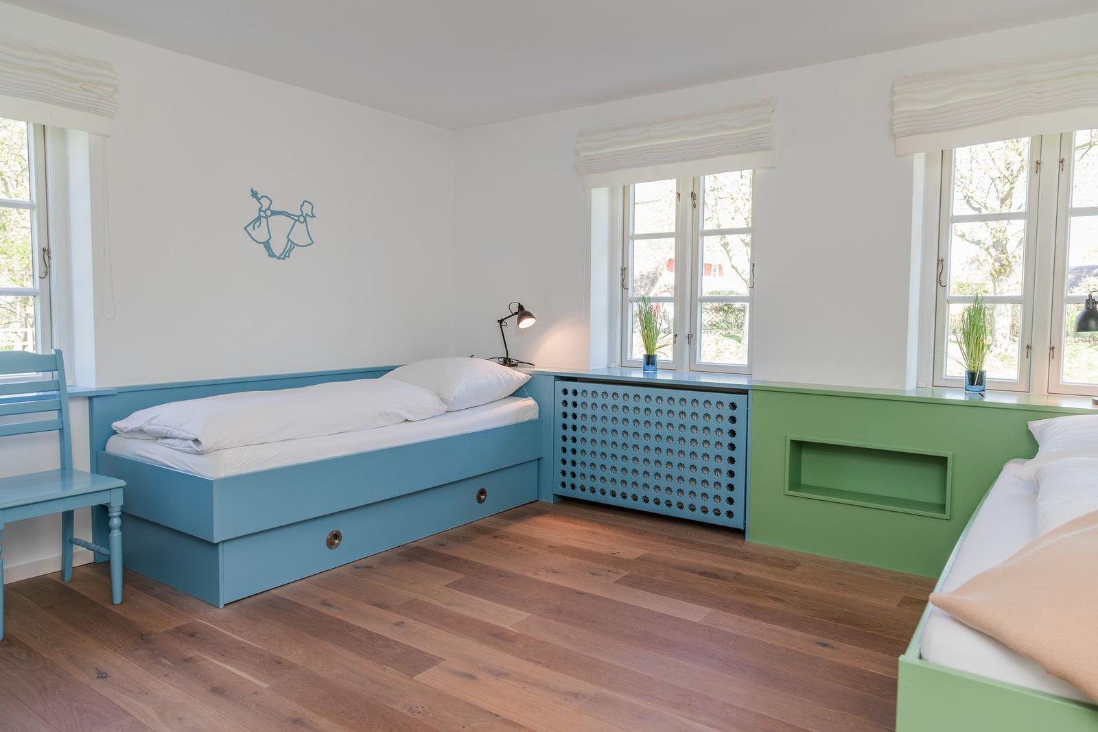 Zimmer mit zwei Betten, Holzboden und Fenstern. Wanddekoration und Nachttische.