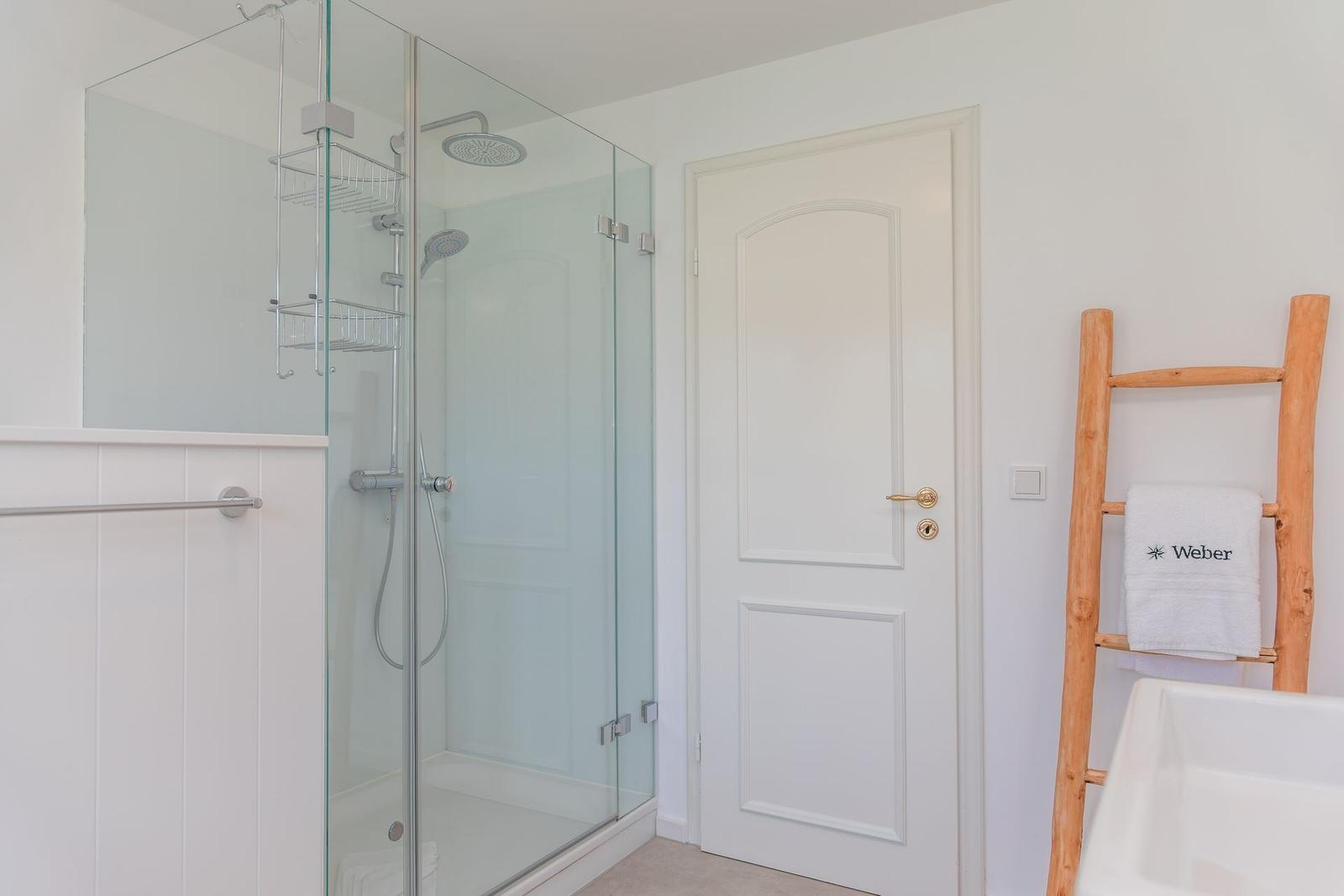 Dusche mit Glaswand, weiße Tür und Holzhandtuchhalter mit Handtuch.