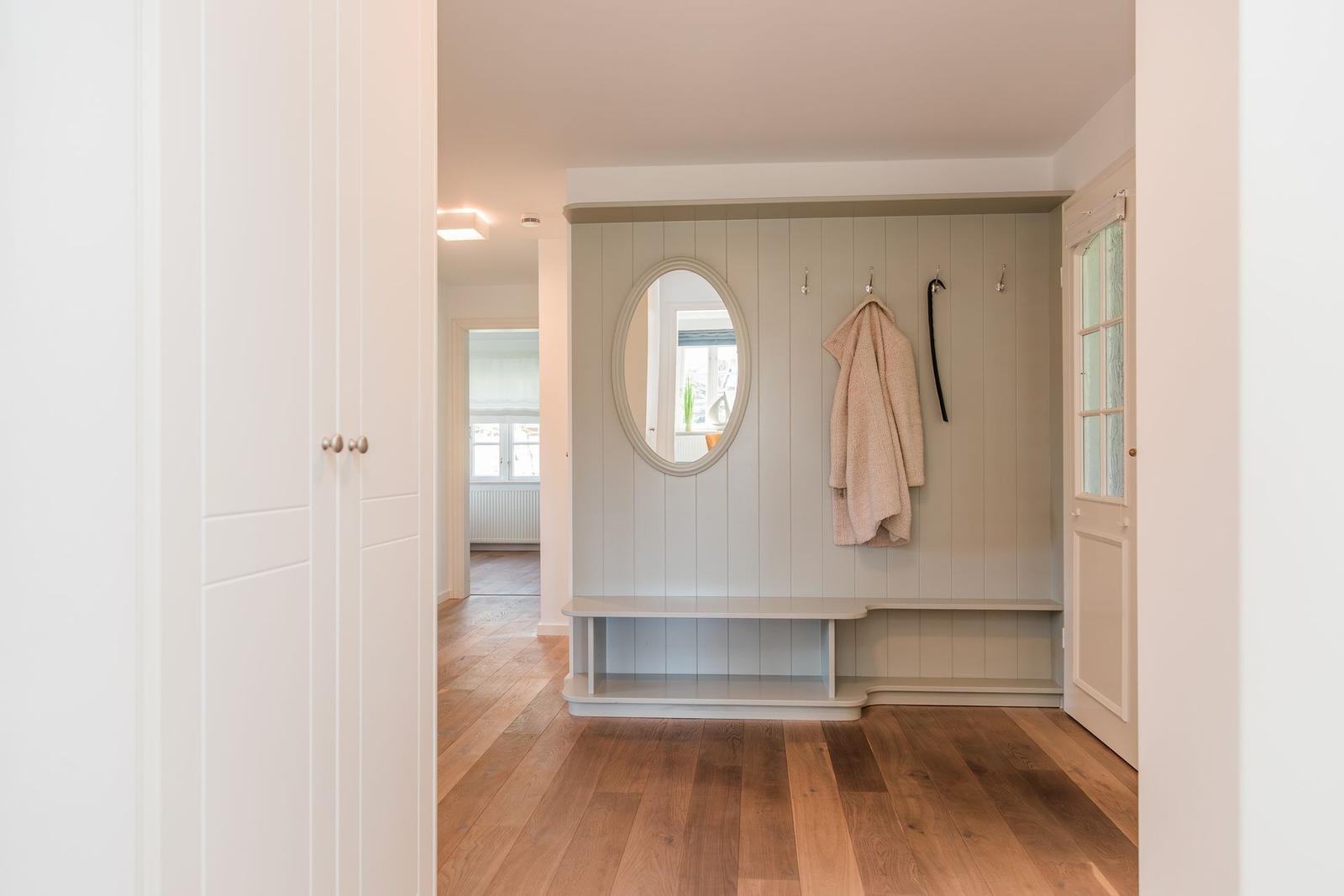 Eingangsbereich mit Spiegelschrank, Haken und Sitzbank. Holzboden und weiße Türen.