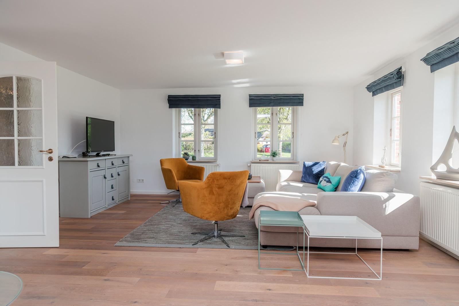 Wohnzimmer mit Sofa, zwei orangefarbenen Sesseln und Fernseher auf Schrank.