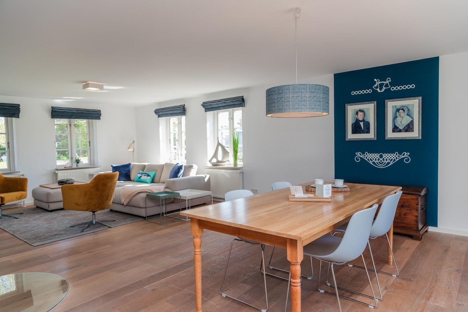 Wohn- und Essbereich mit Holzboden, Sofa, Esstisch und blauer Wand mit Bildern.