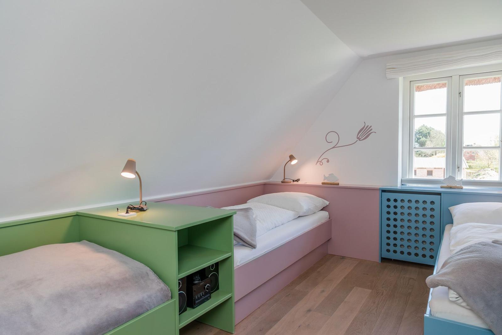 Zimmer mit zwei Betten, Fenster und Holzboden. Wanddekoration und Nachttische.