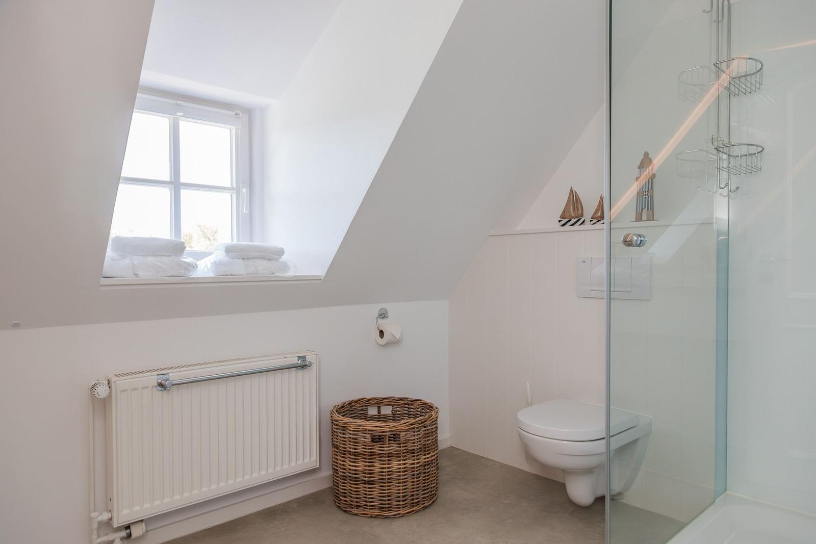 Badezimmer mit Dusche, Toilette und Fenster mit Handtüchern.