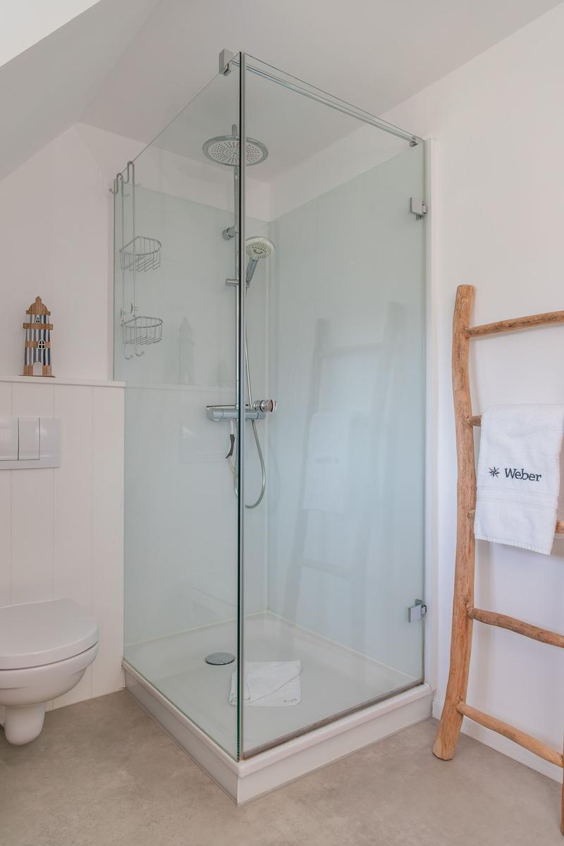 Dusche mit Glaswand, Toilette und Holzhandtuchständer.