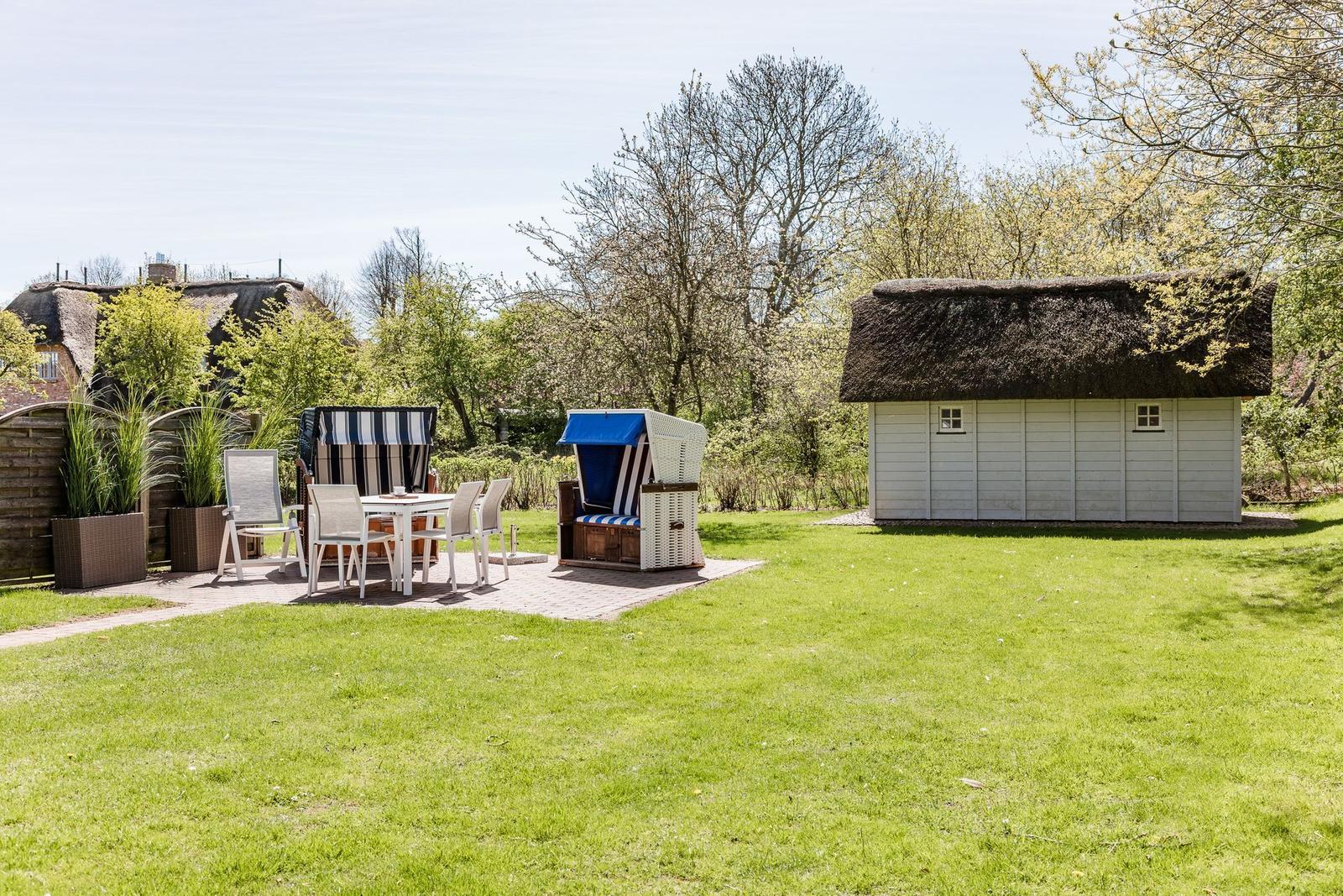 Garten mit Terrasse, Strandkörben und strohgedecktem Schuppen.