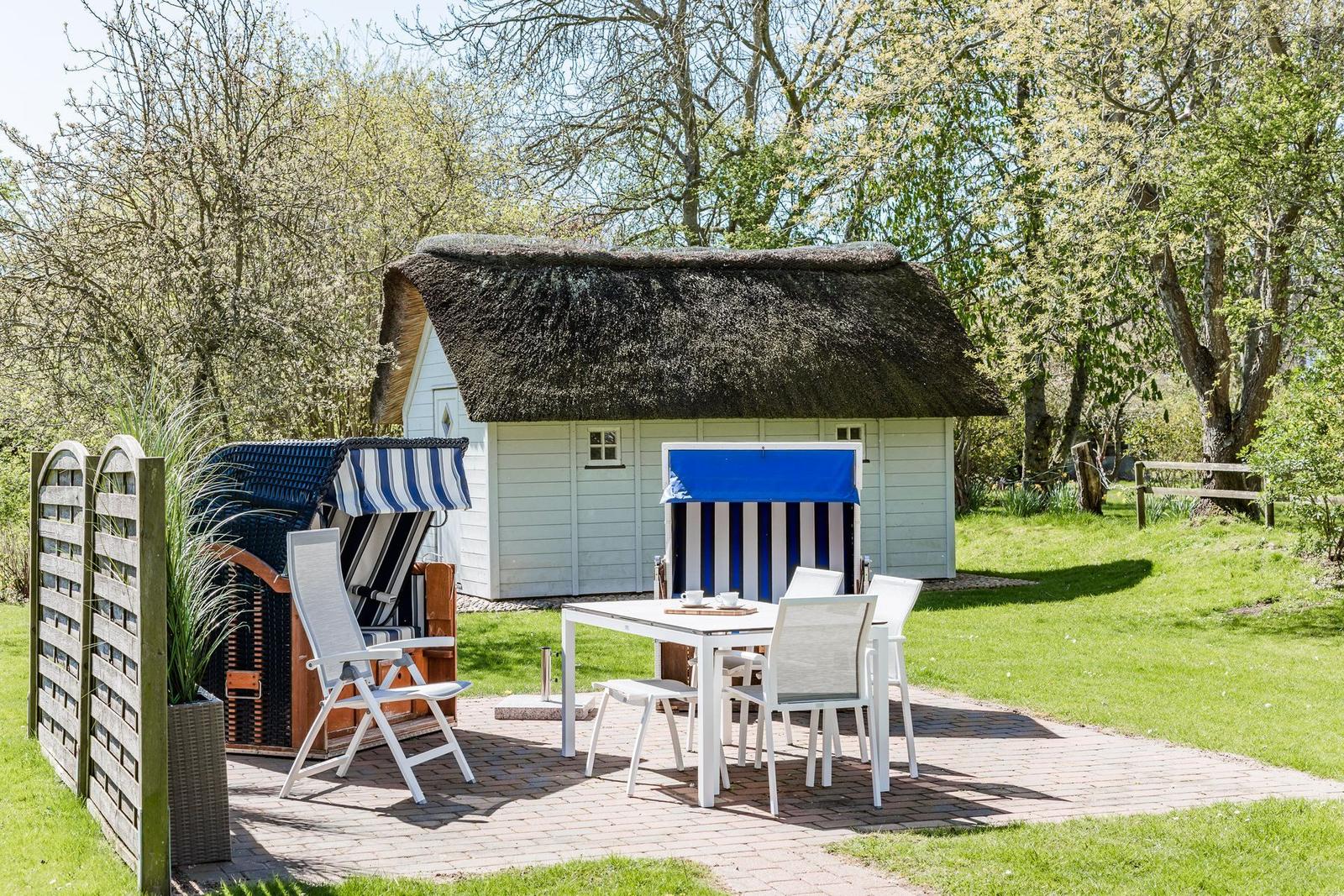 Terrasse mit Tisch, Stühlen und Strandkörben vor einem Haus mit Strohdach.