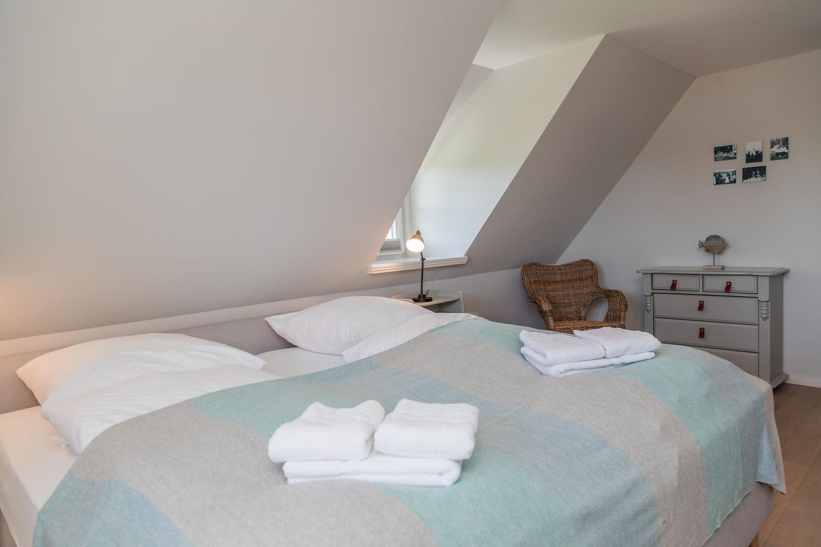 Schlafzimmer mit Dachschräge, Bett, Nachttisch, Stuhl und Schrank.