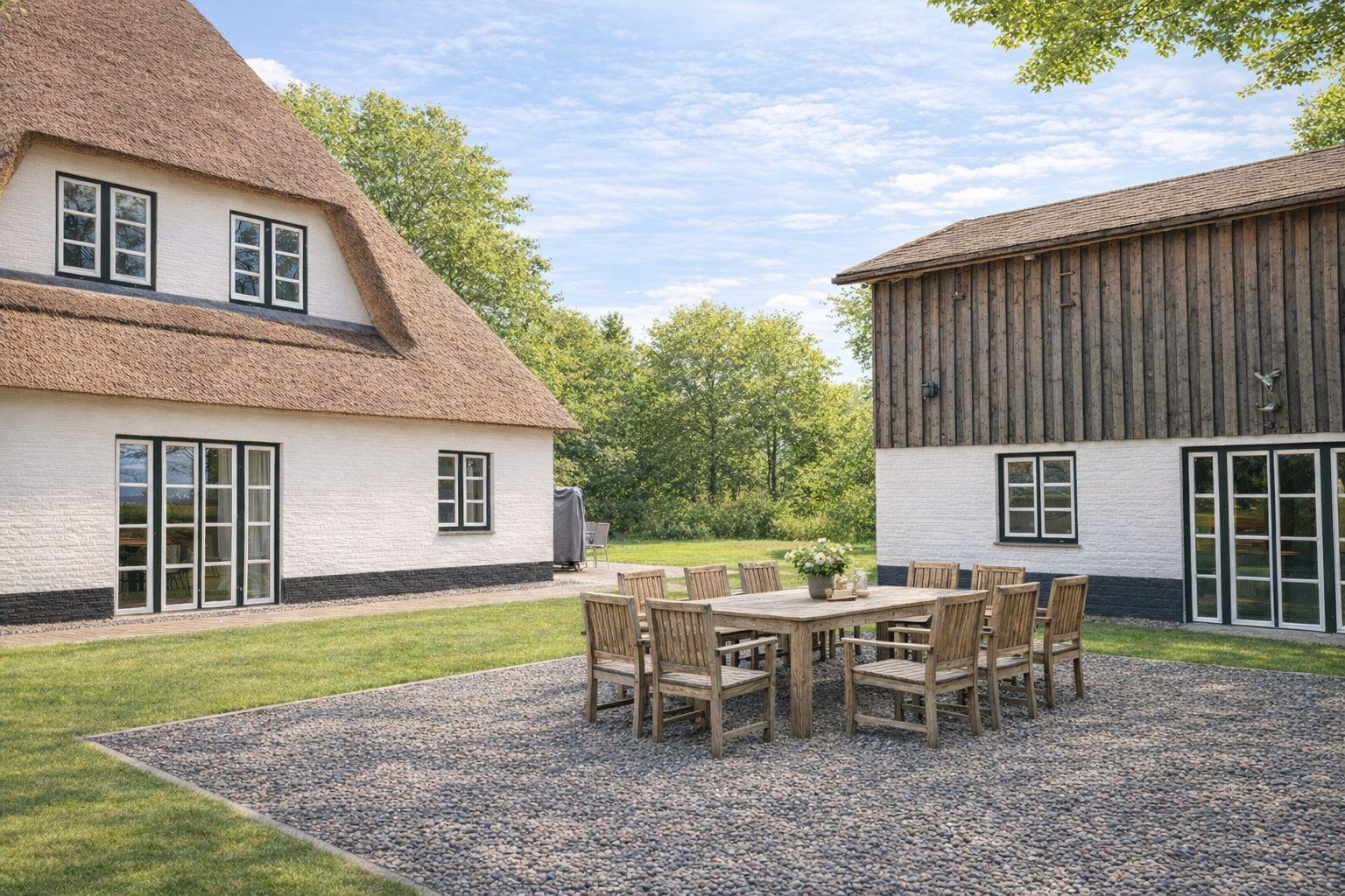 Haus mit Strohdach und Holzschuppen. Außenterrasse mit Tisch und Stühlen.