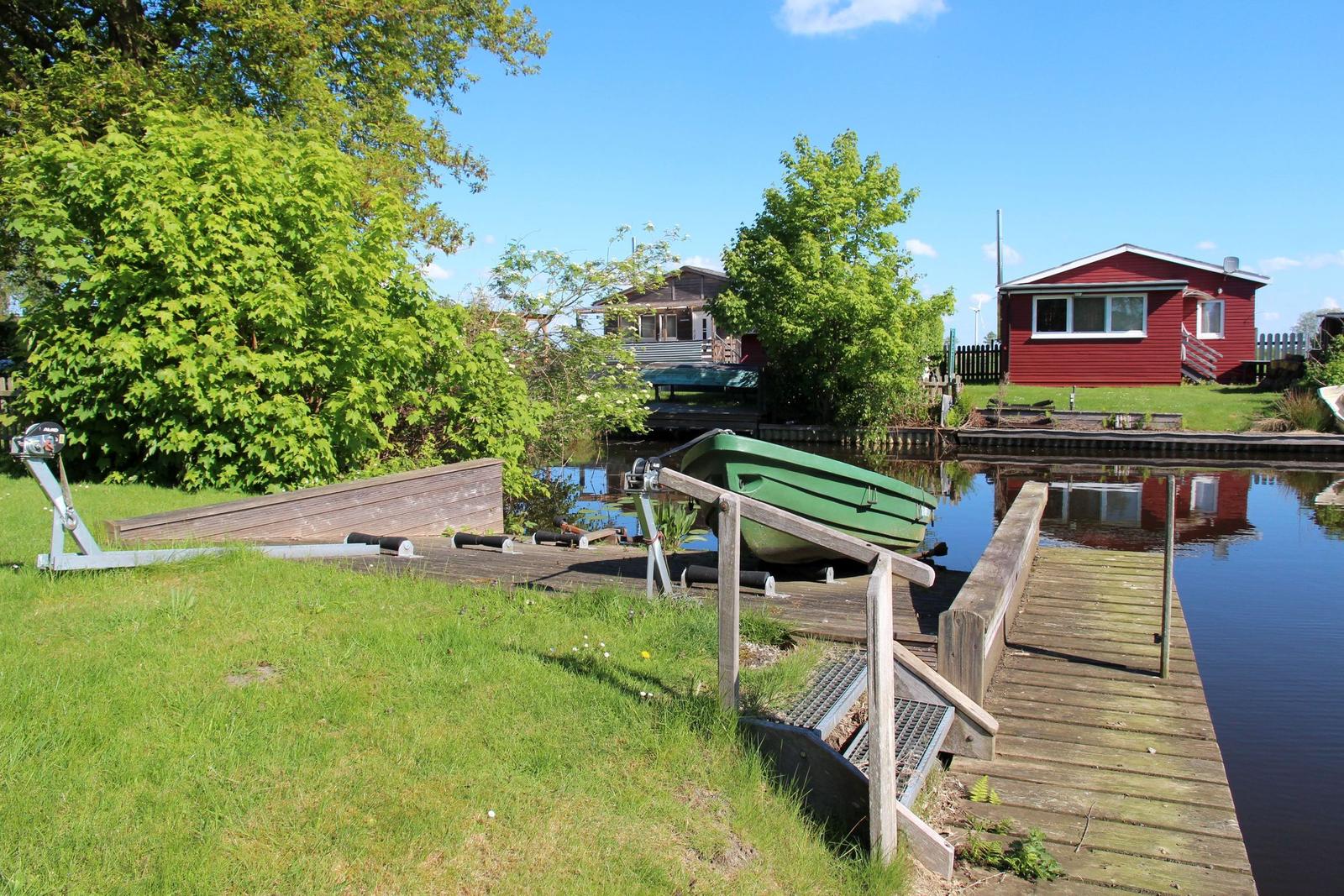 Wooden dock with boat on canal, green trees and red house in background.