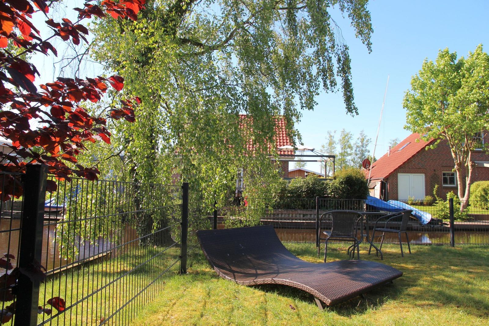 Garden with lounge chair and table, surrounded by trees and a fence.