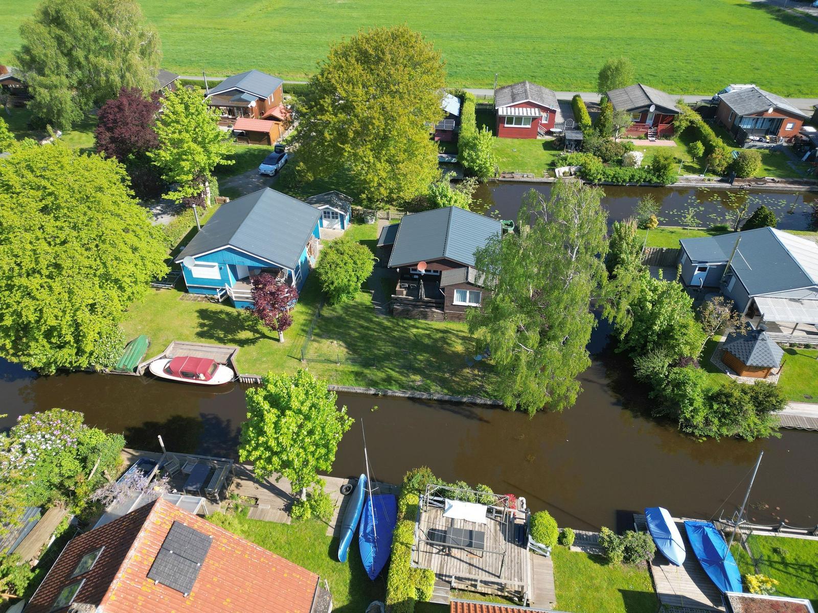 Aerial view of canal houses with boats and green lawns.