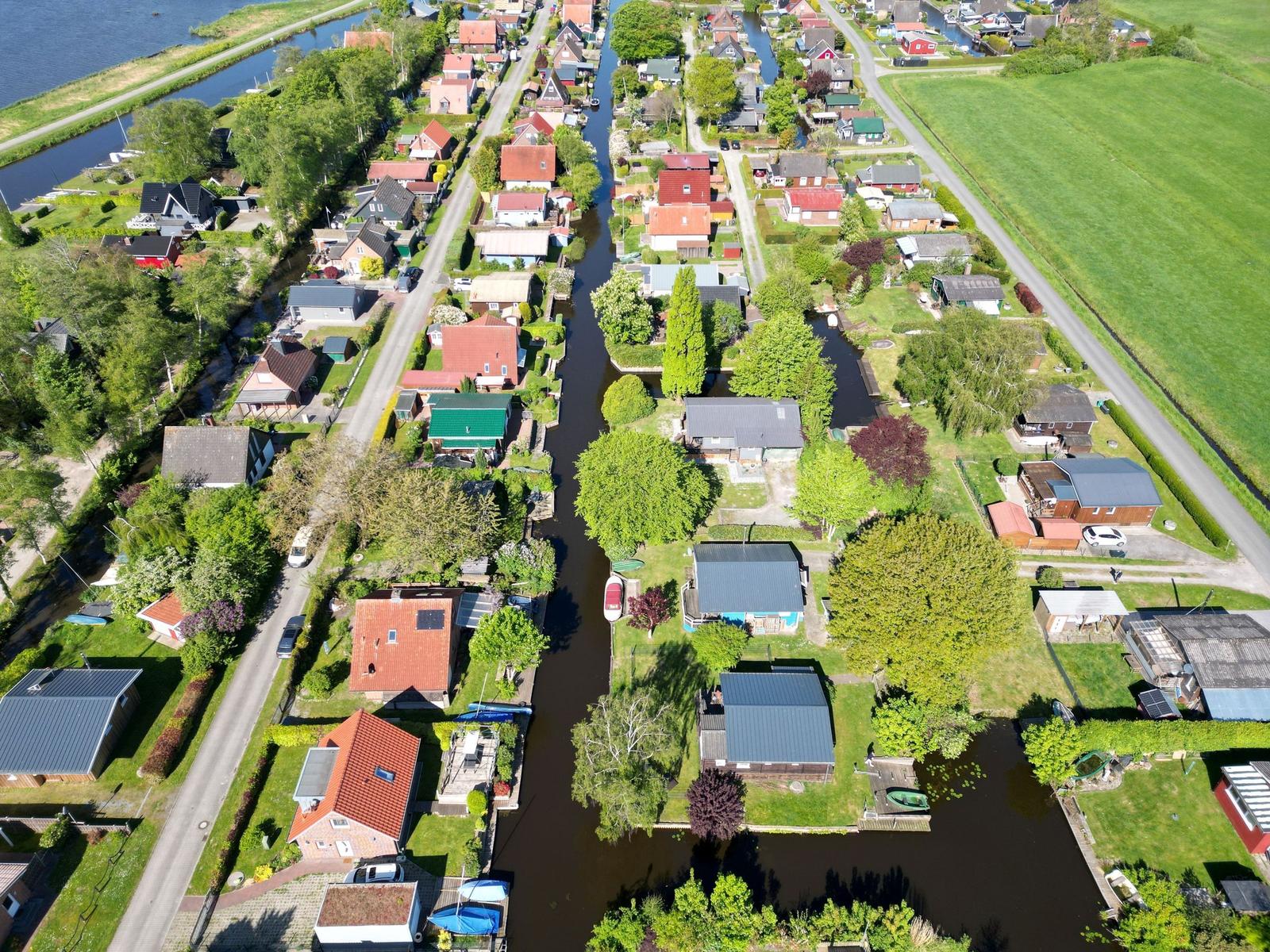 Aerial view of a village with houses along a canal and green fields.