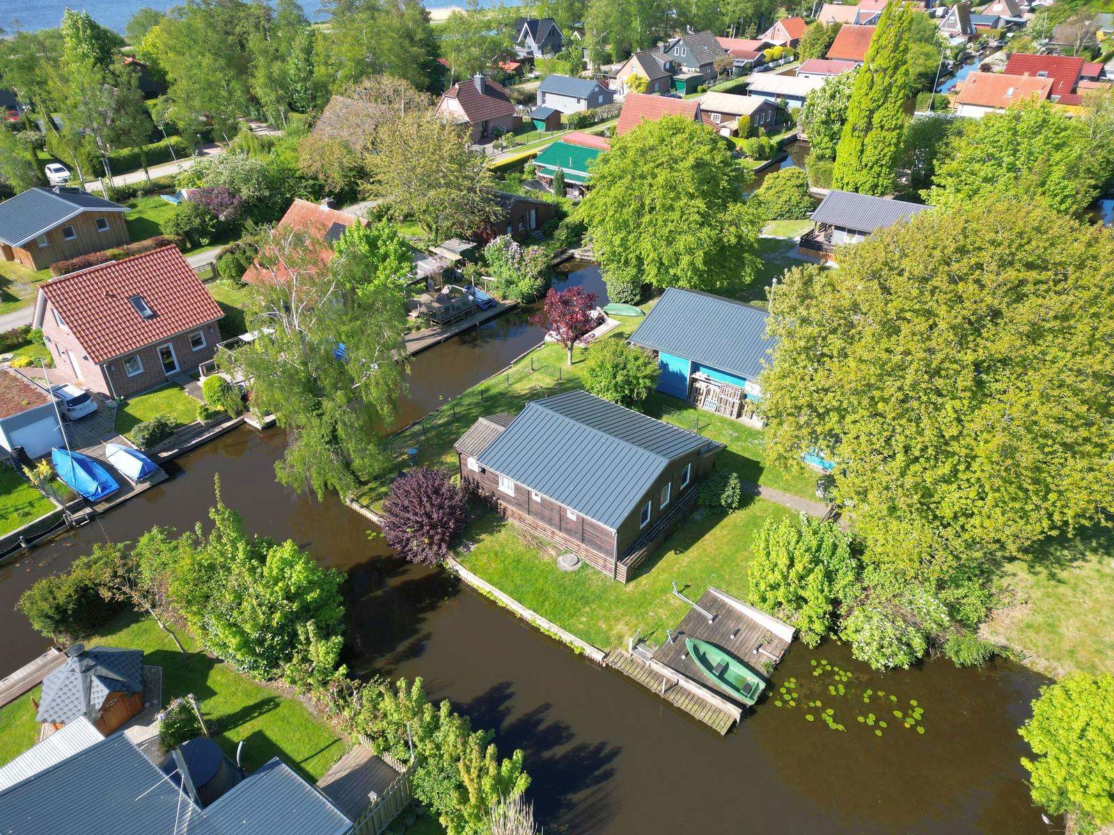 House with boat dock on canal, surrounded by trees and other houses.