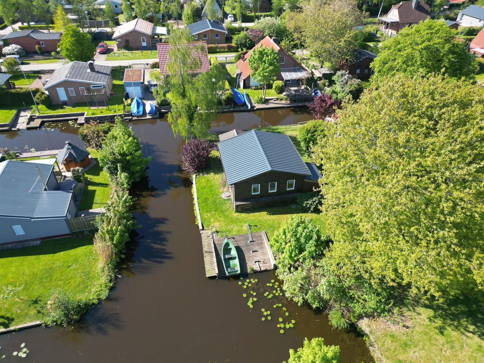 House by canal with boat and green surroundings