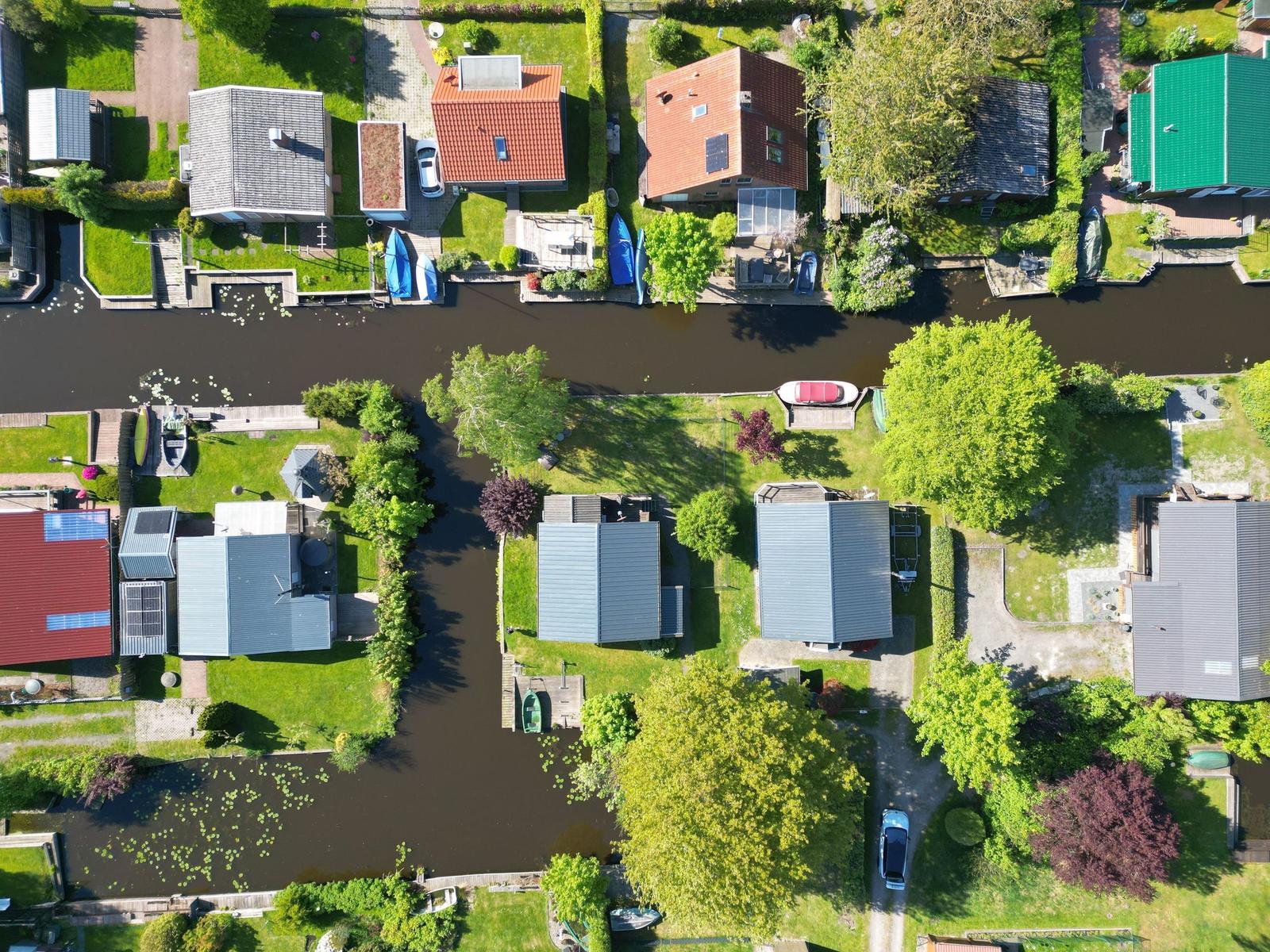 Aerial view of houses along a canal with boats and green areas.