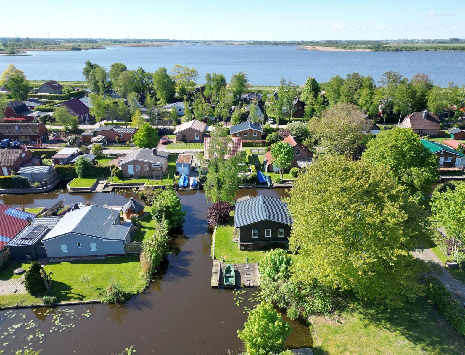 House with boat dock on canal, surrounded by green areas and water.