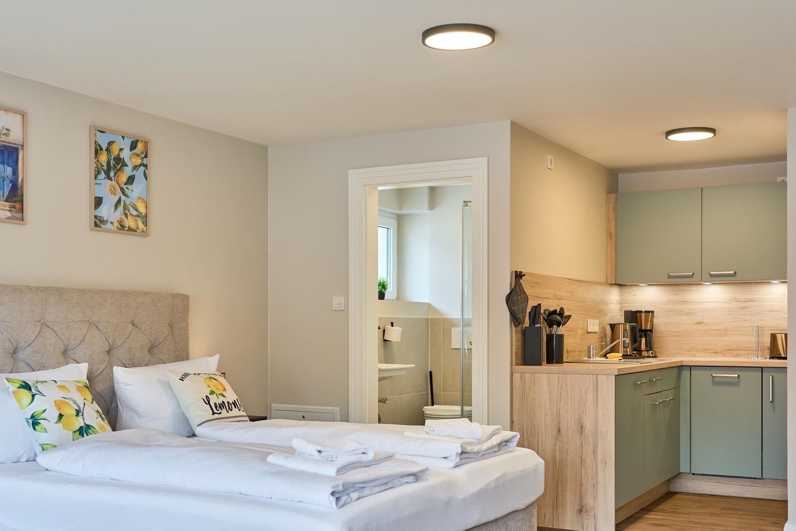 Schlafzimmer mit Bett und Küche. Badezimmer im Hintergrund sichtbar.