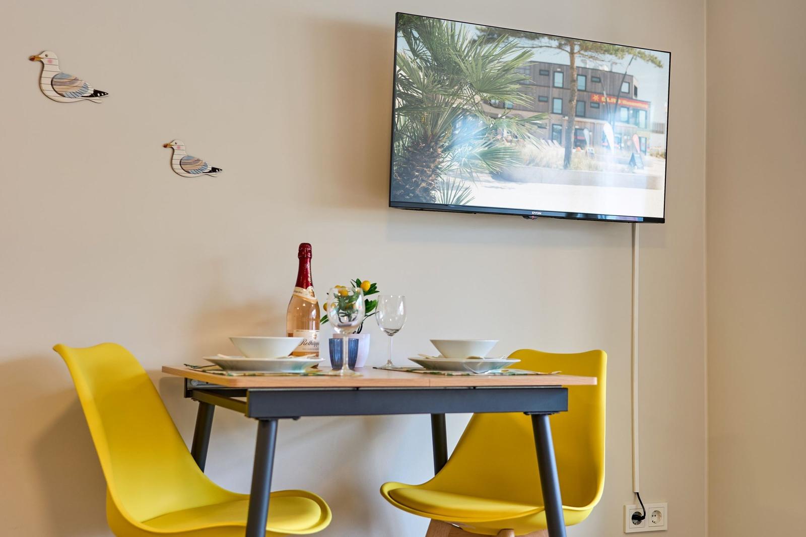 Esstisch mit zwei gelben Stühlen, Fernseher und Wanddekoration mit Möwen.