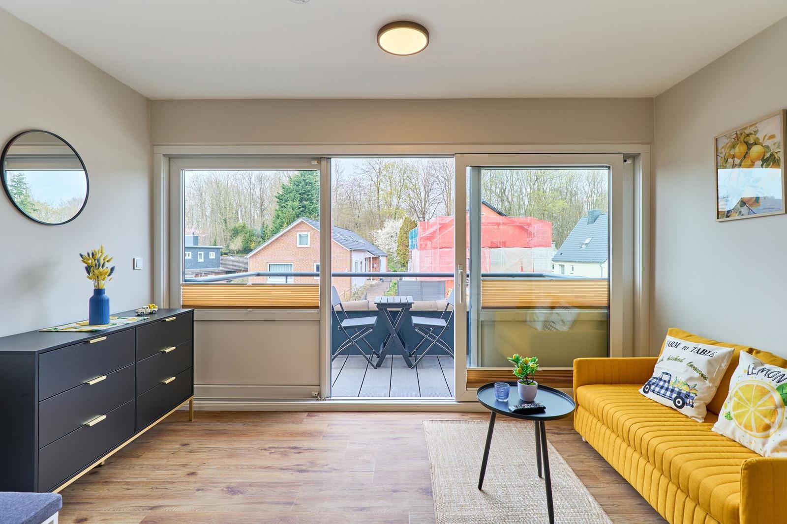 Wohnzimmer mit gelbem Sofa, Balkon und Holzboden.