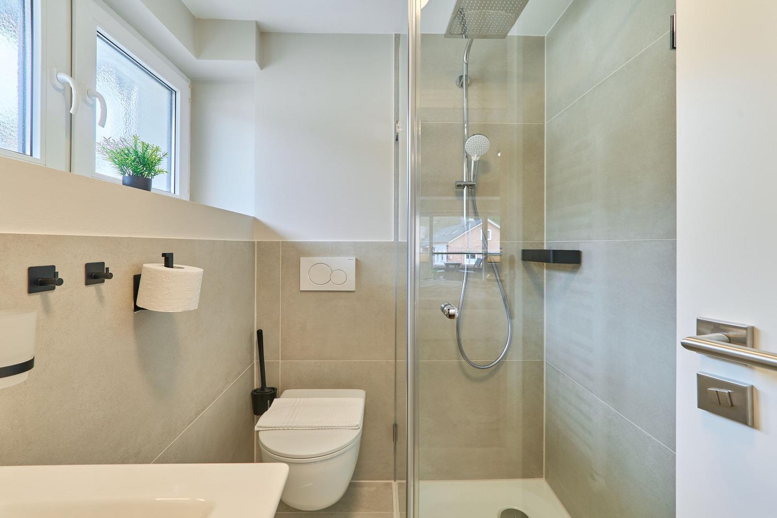 Bad mit Dusche, Toilette und Fenster mit Pflanze.
