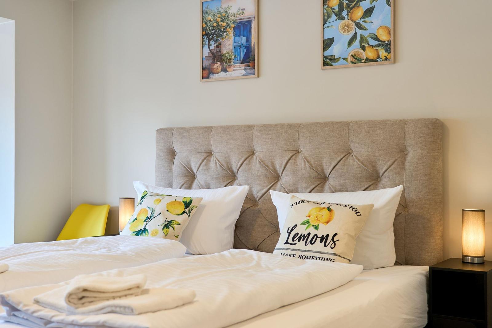Schlafzimmer mit Bett, Kopfkissen und Wandbildern mit Zitronenmotiv.