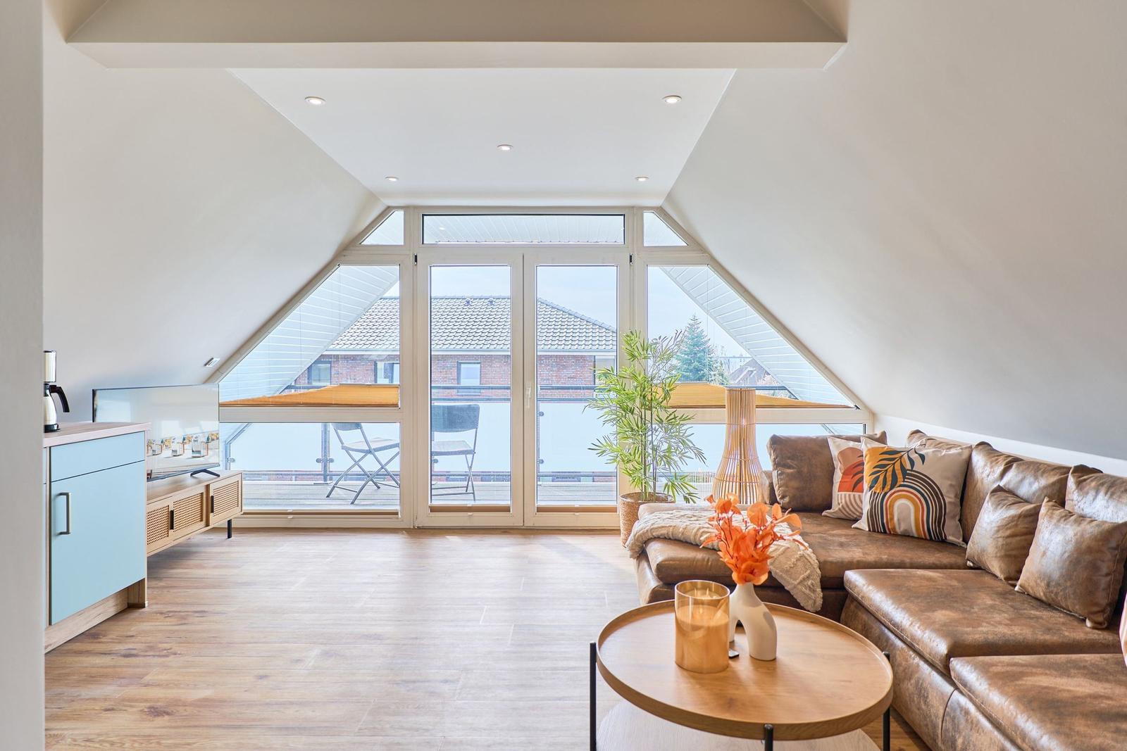 Wohnraum mit braunem Sofa, Glasfront und Holzboden. Blick auf Balkon und Nachbarhäuser.