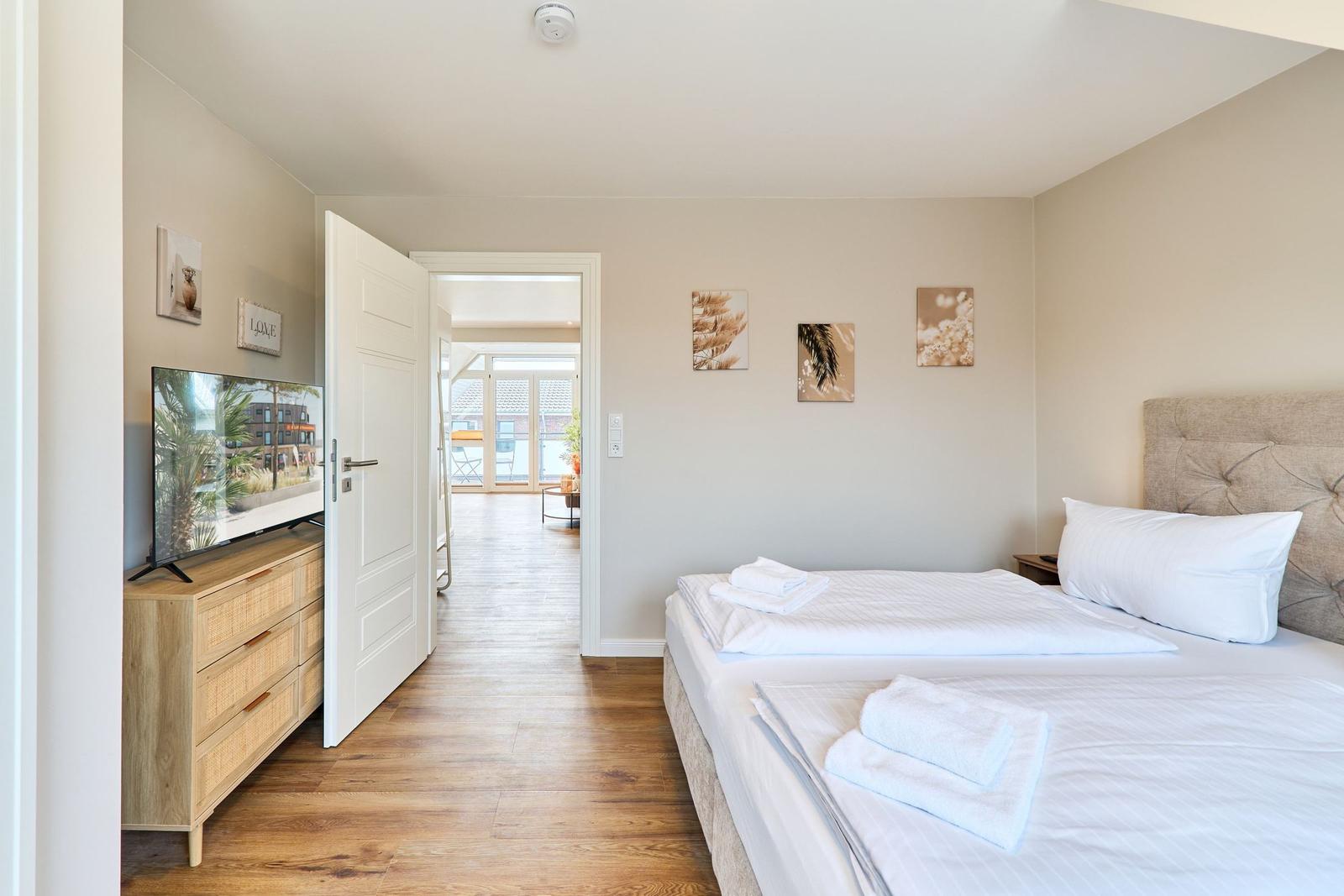 Schlafzimmer mit Bett, Fernseher und Blick in Wohnbereich.