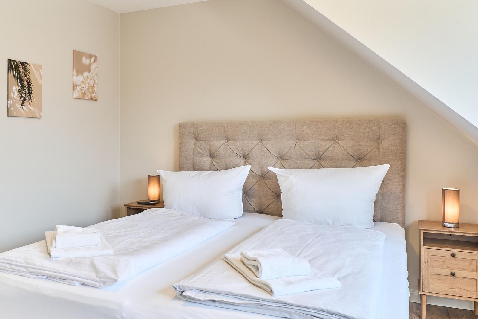 Schlafzimmer mit Doppelbett, zwei Nachttischen und Wandbildern.