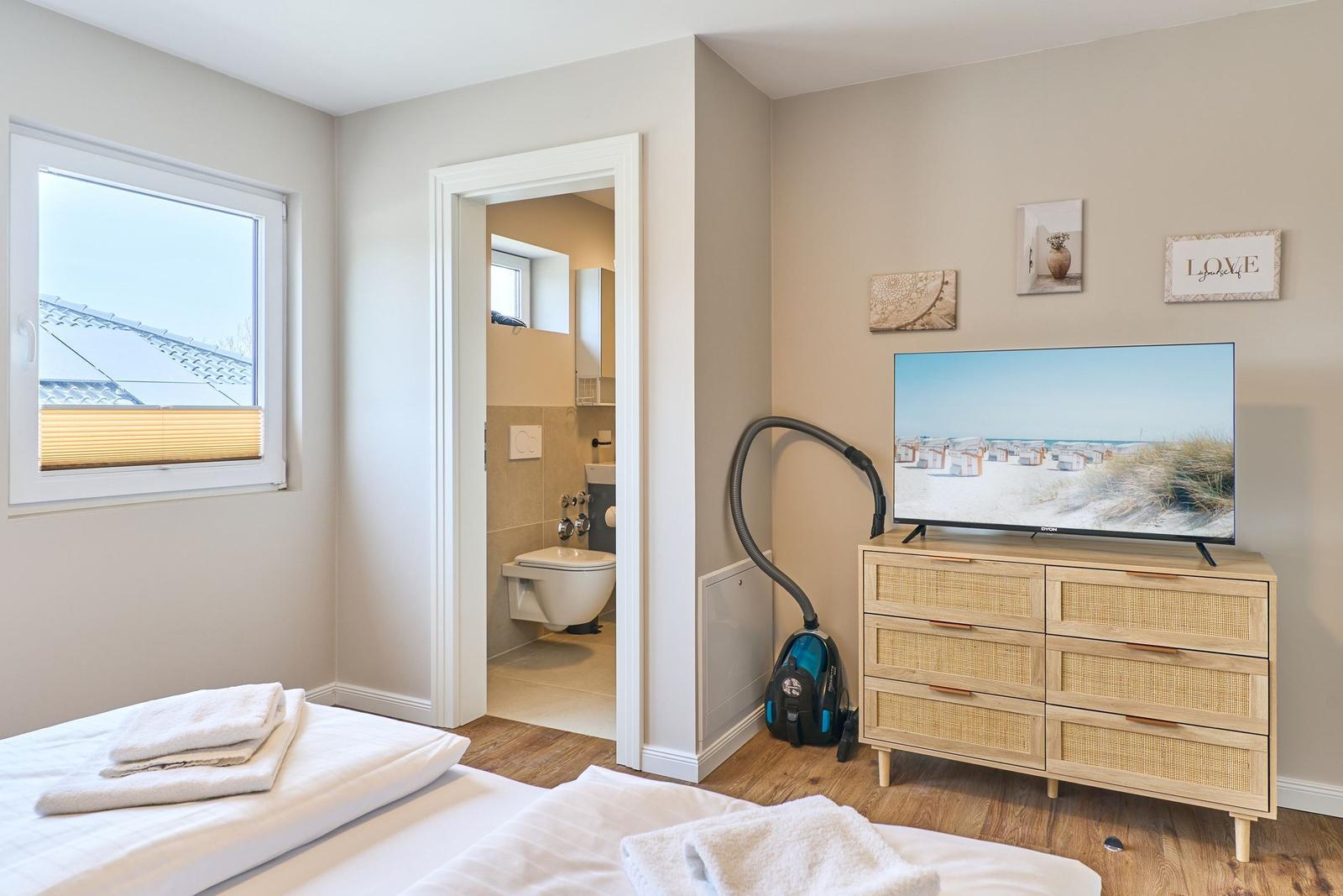 Schlafzimmer mit TV, Schrank und Bad im Anschluss.