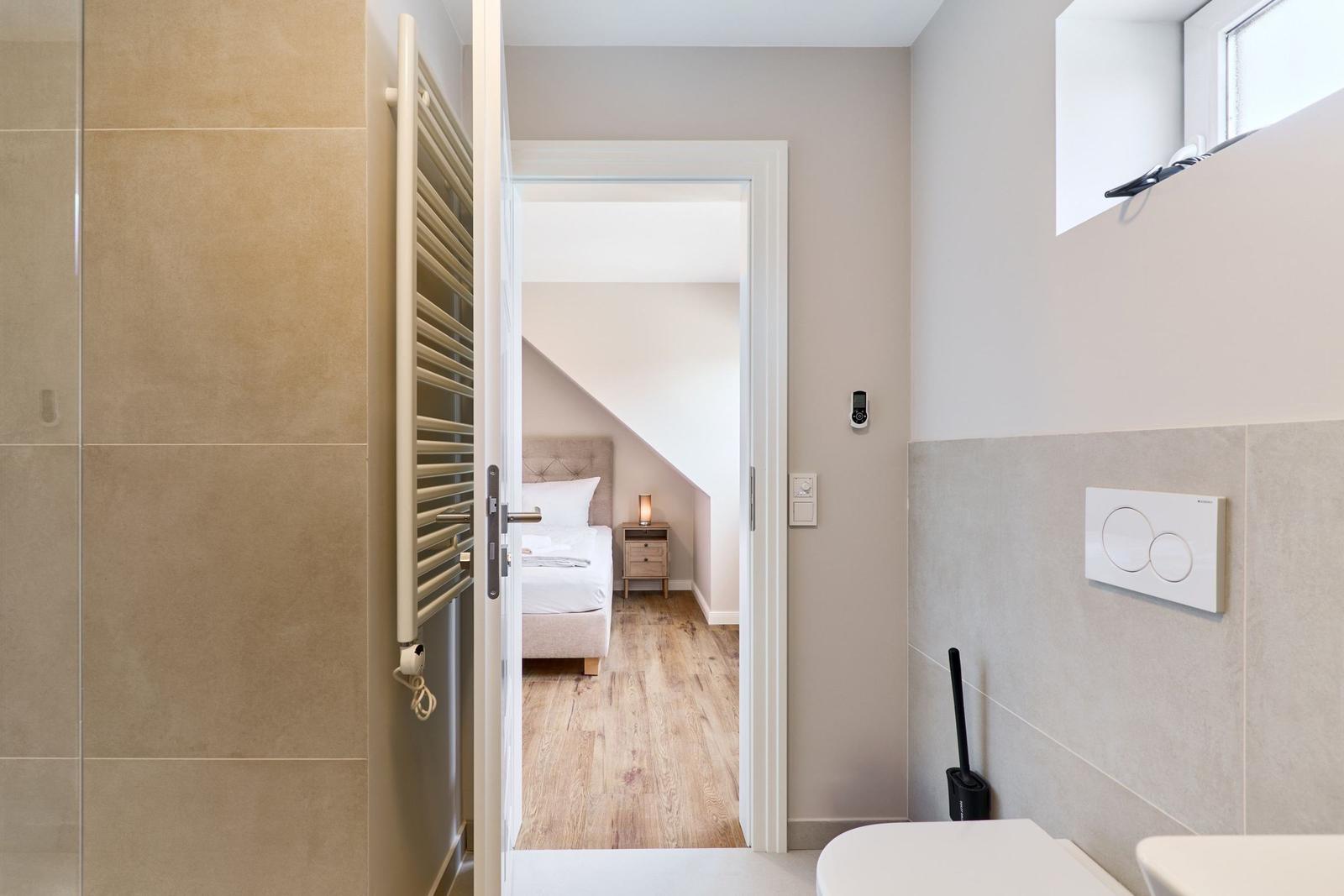Badezimmer mit Tür zum Schlafzimmer mit Bett und Nachttisch